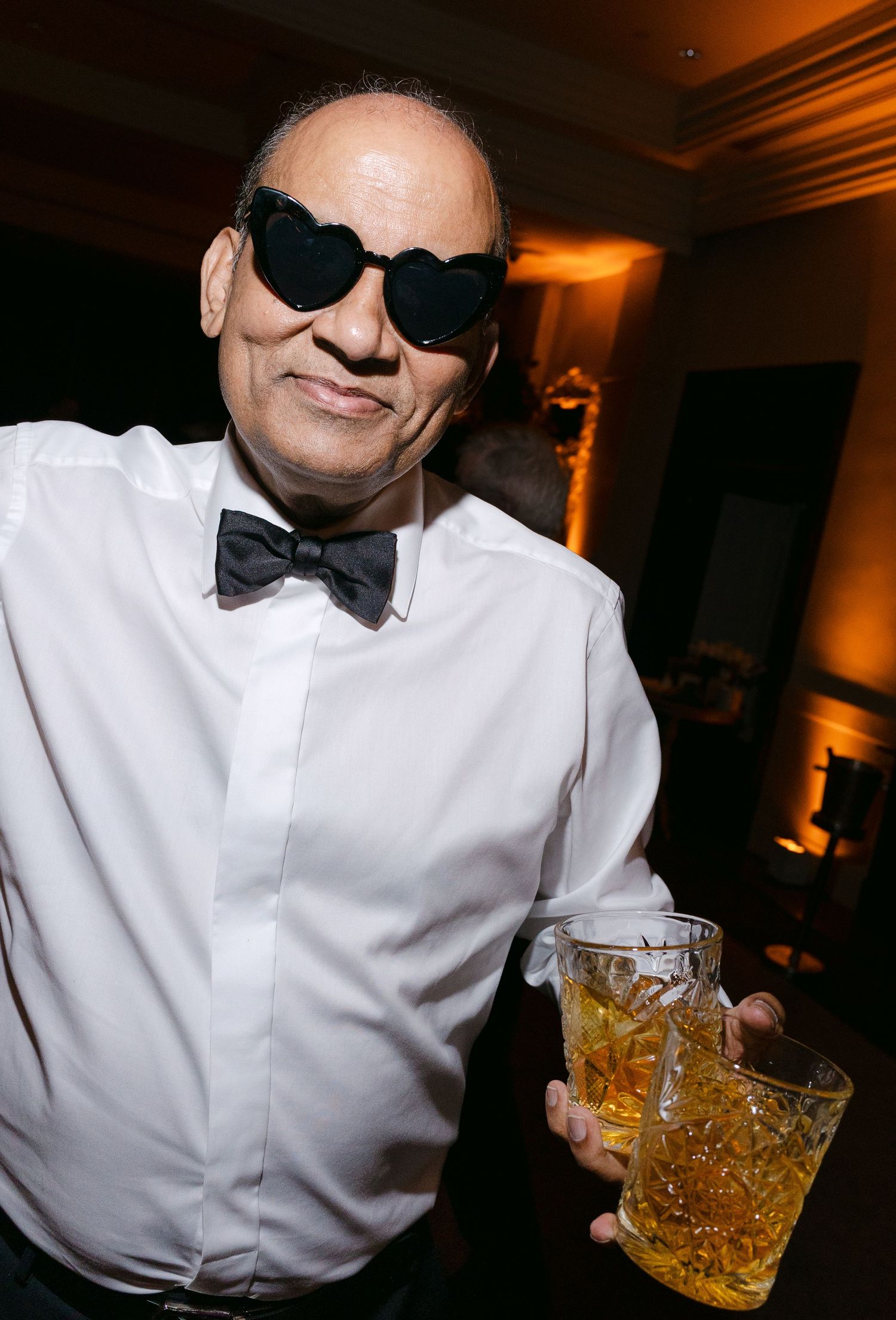 Server in formal attire with bowtie holding cocktails at an event.
