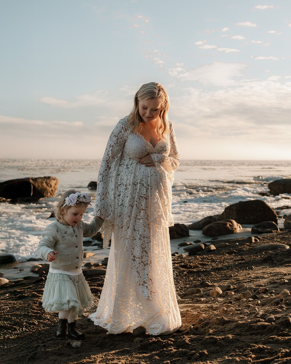 En gravid kvinna som går på en stenig strand tillsammans med en liten flicka. De går hand i hand och i bakgrunden är det is och vatten.