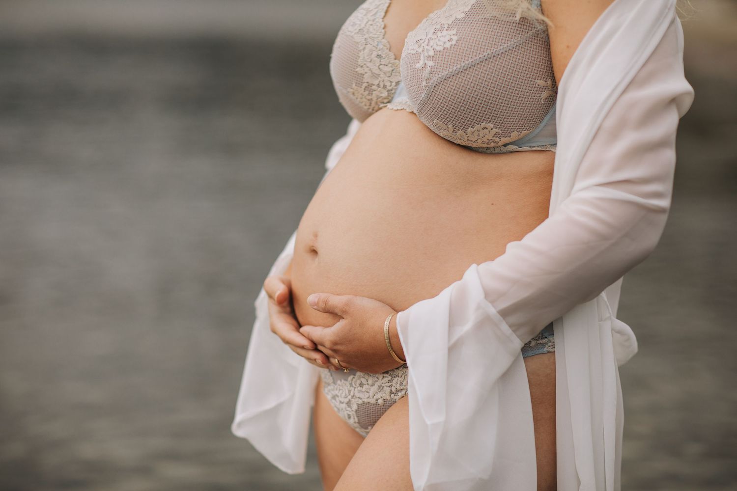 En gravid kvinna som står i vatten och håller sina händer på magen.