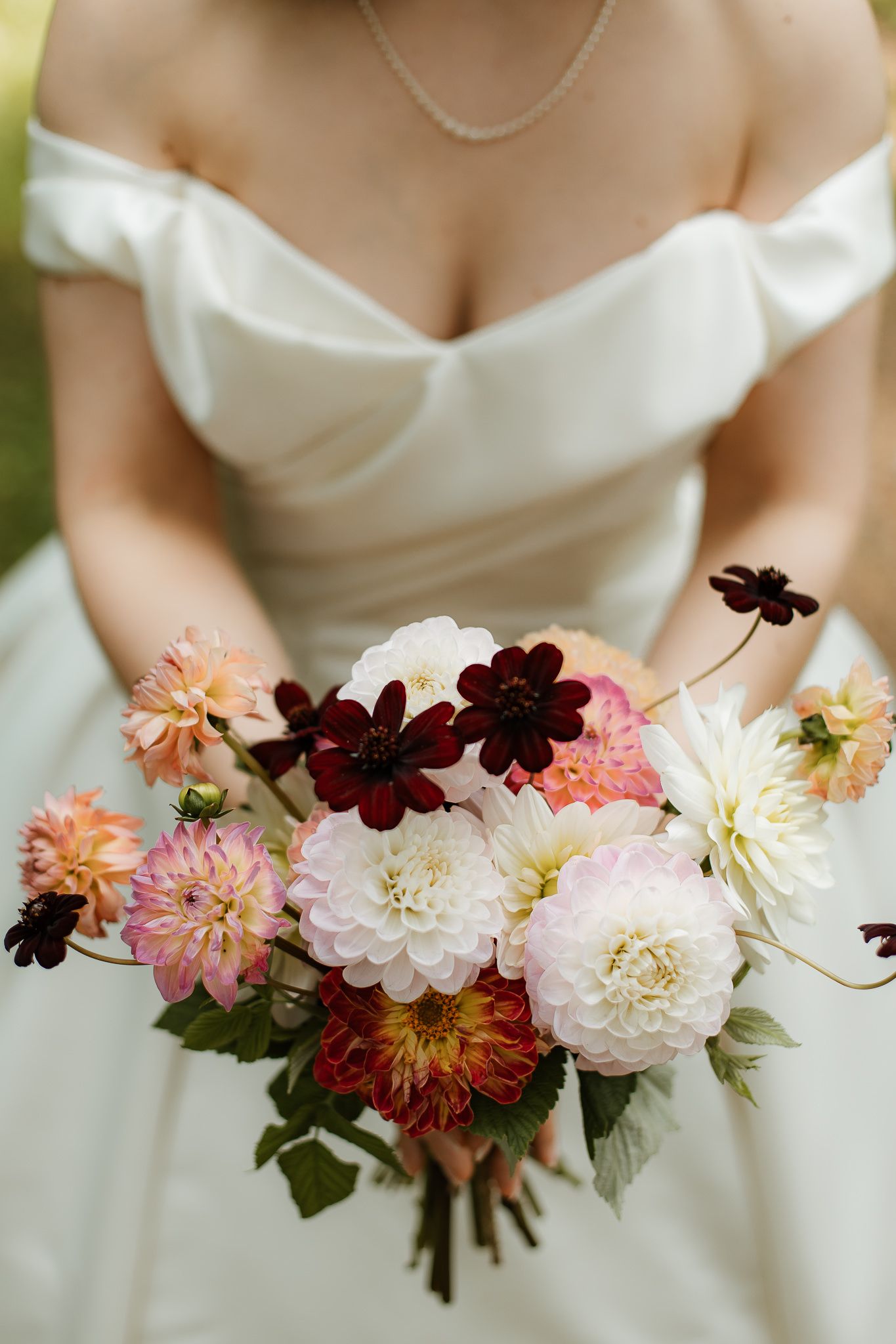 Närbild på ett par kvinnohänder som håller i en färggrann brudbukett med blandade sommarblommor.