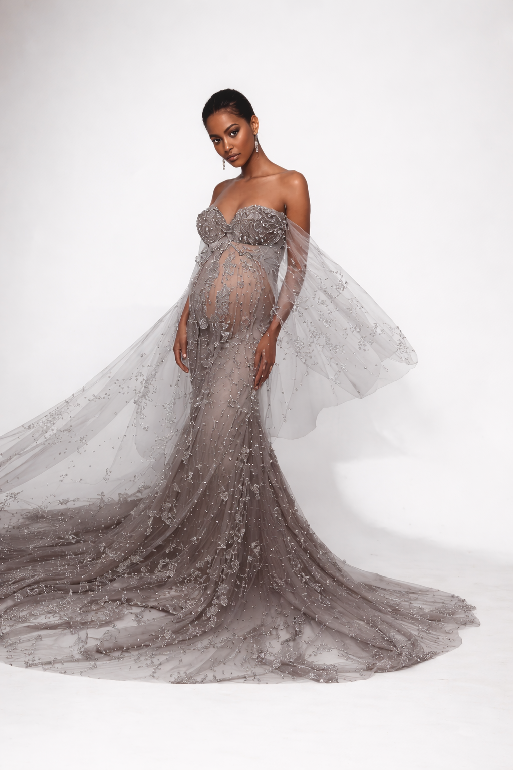 A stunning off-shoulder evening gown in shimmering grey tulle with intricate beading and a dramatic flowing train.