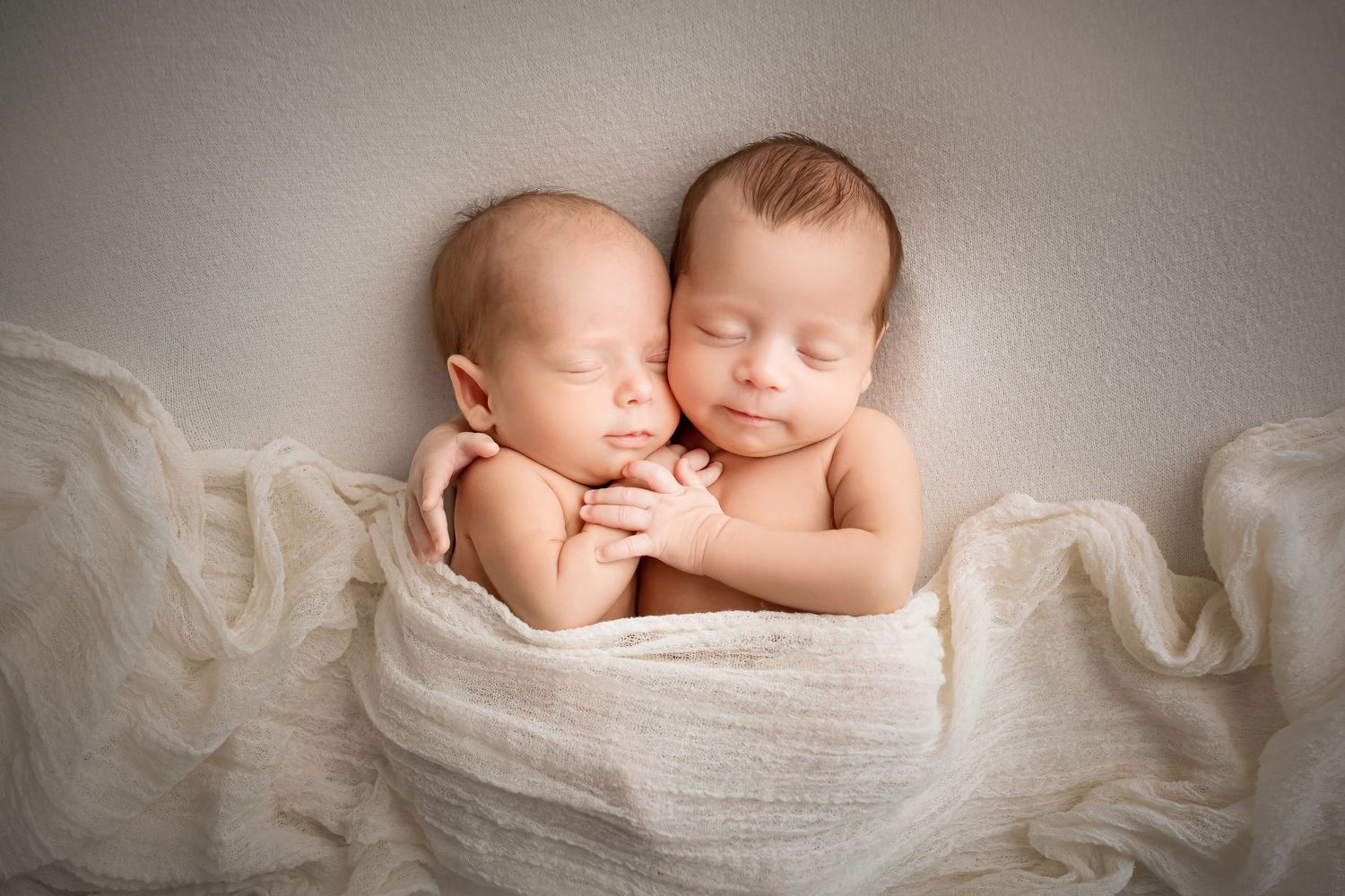 Peaceful sleeping newborn baby wrapped in soft white fabric lying on textured backdrop.