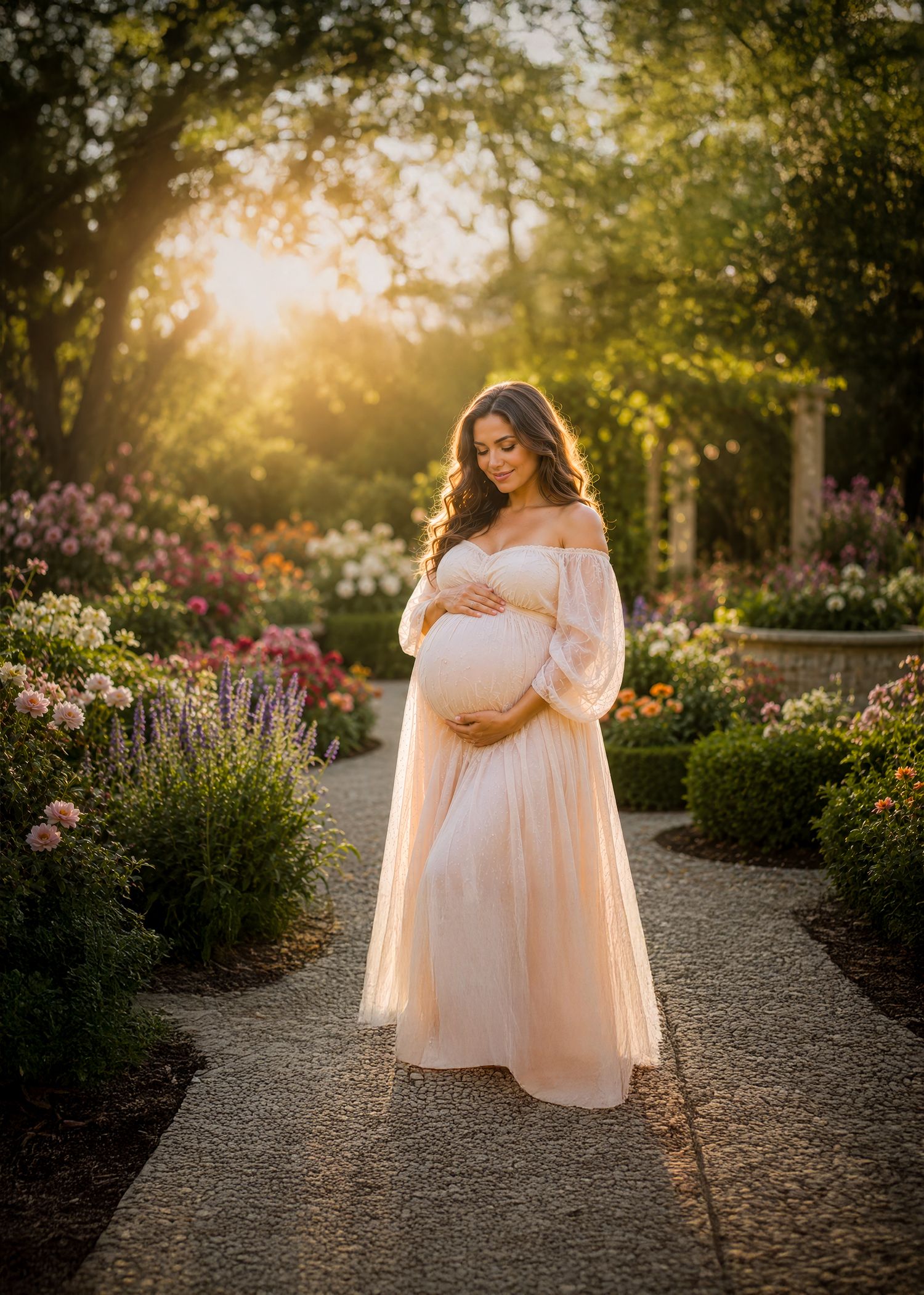 Pregnant woman in blush off-shoulder gown cradles belly in sunlit garden with colorful blooms.