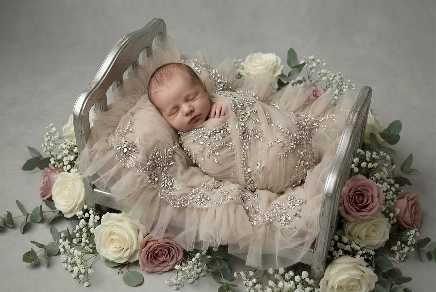 A newborn baby sleeps peacefully in a floral setting with pink roses and eucalyptus leaves surrounding them.