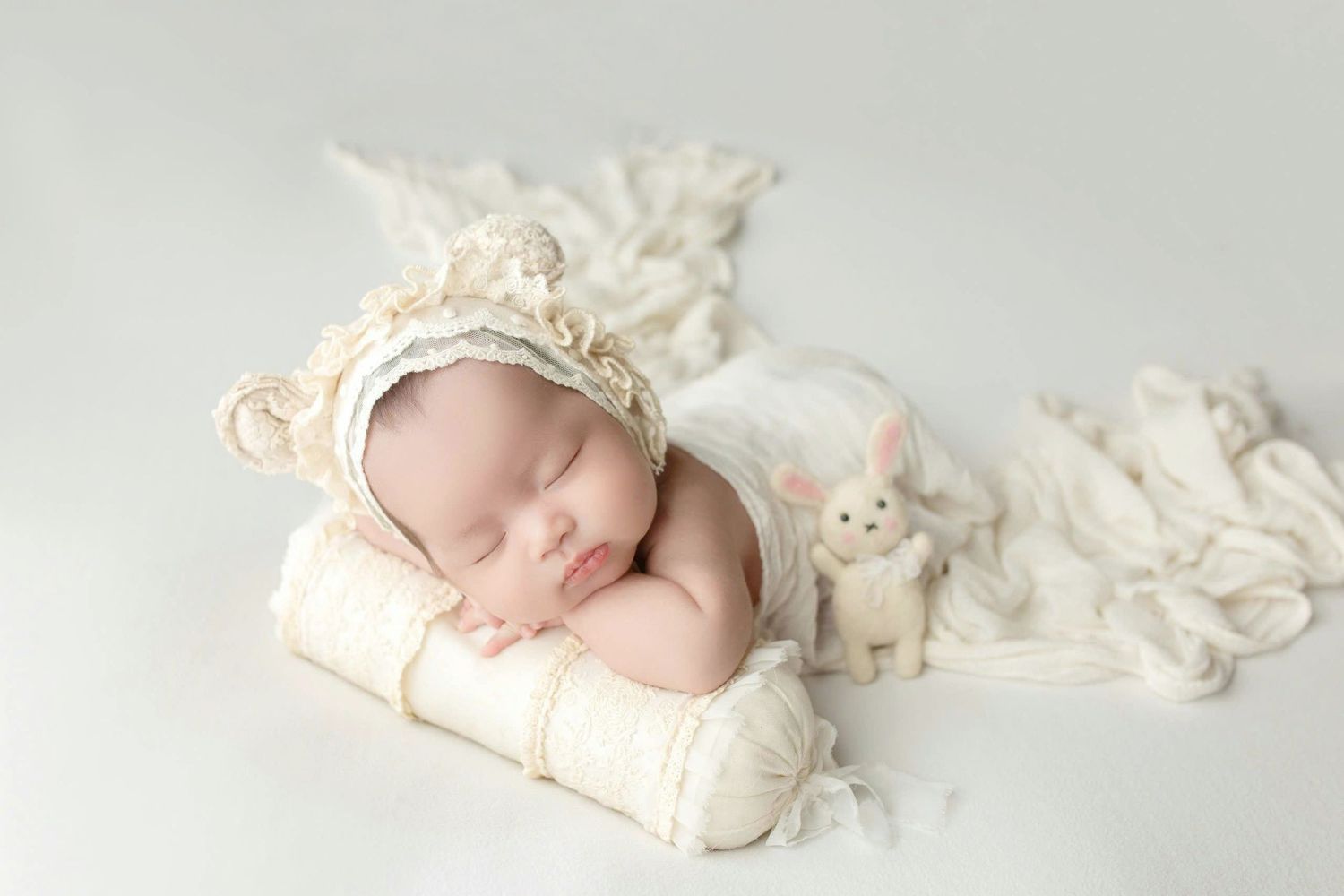 A baby sleeps peacefully in soft white blankets during a professional newborn photography session.