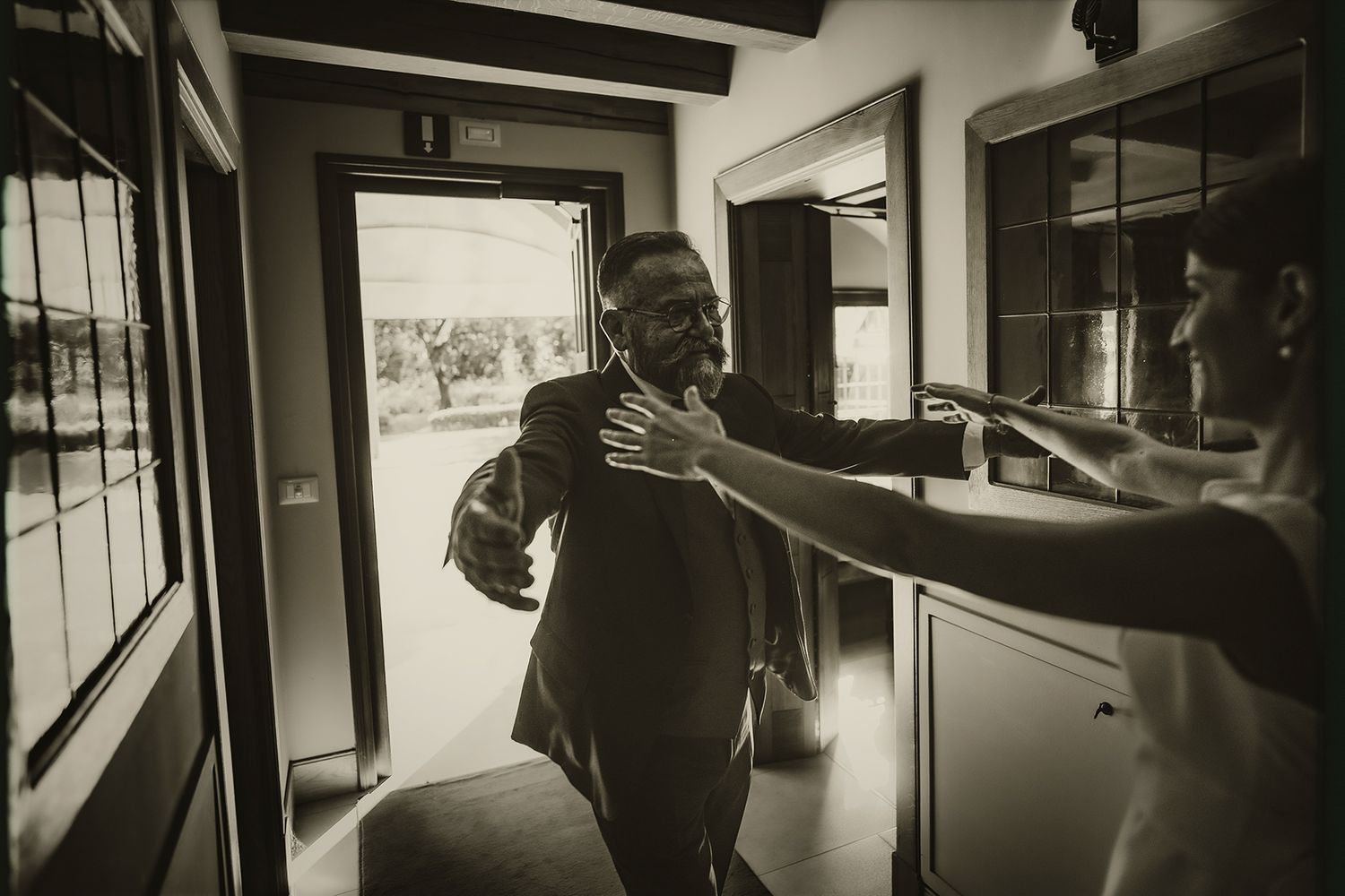 A black and white candid photo shows people interacting in a hallway near a bright window.