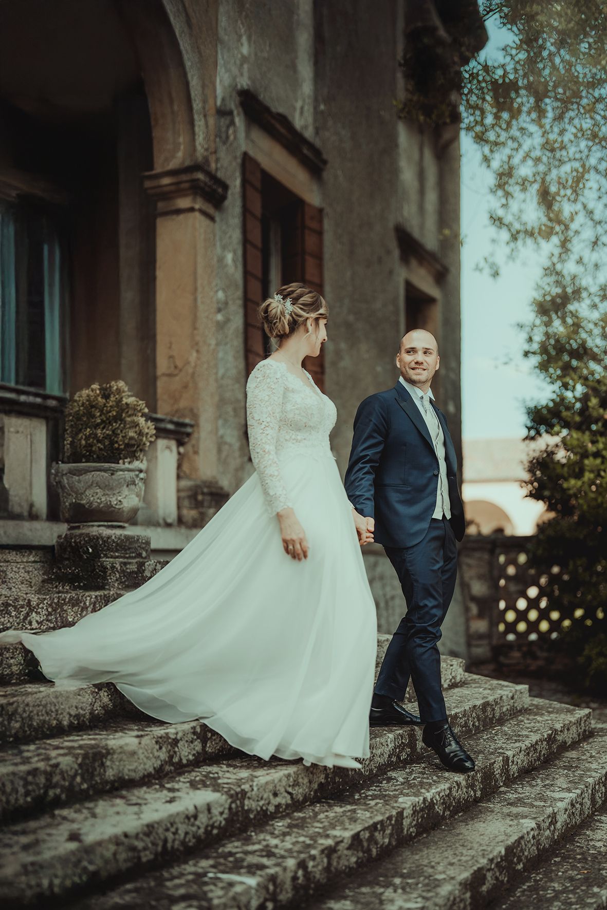 A flowing white wedding dress twirls gracefully on stone steps against a historic building backdrop.