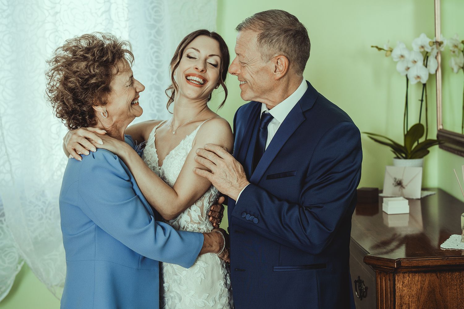 Emotional wedding moment captured in soft green tones with natural window light.