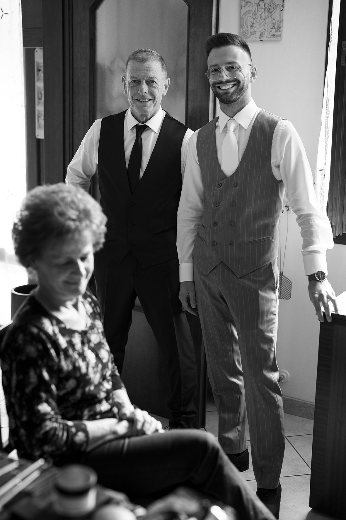 Black and white candid photo of three people in formal attire standing in hallway.