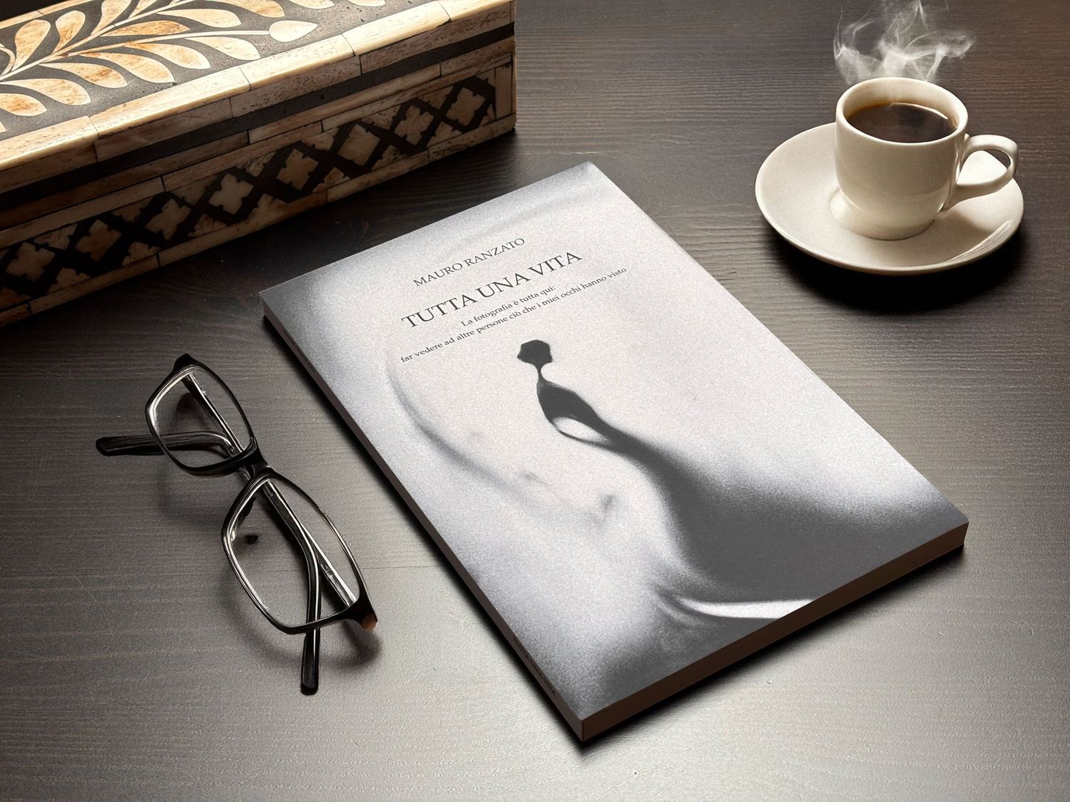 Coffee cup and glasses next to an elegant wedding photo album on dark wooden table.