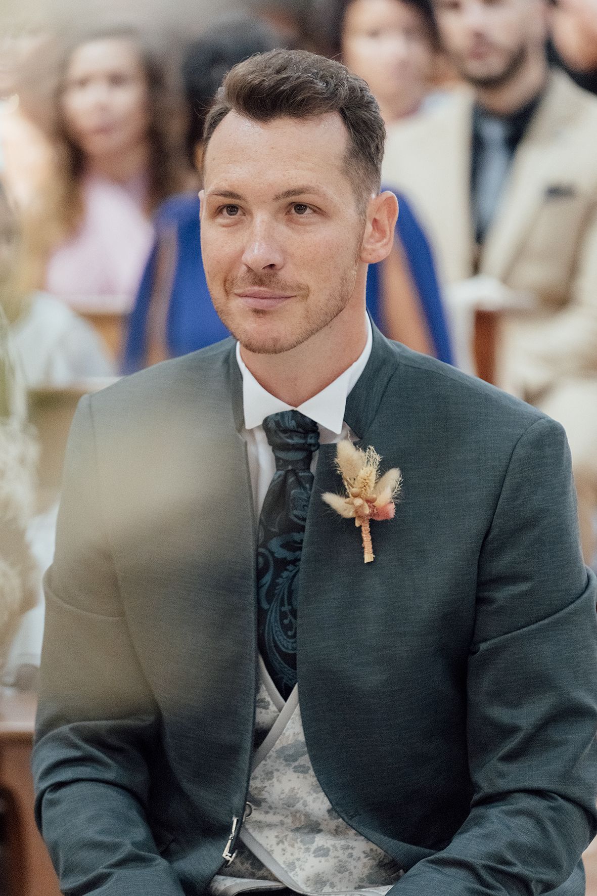 Groom in dark suit smiles warmly during wedding ceremony.