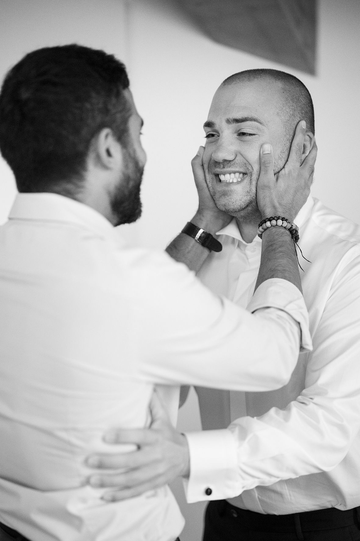 Two men in white shirts share an emotional moment before a wedding ceremony.