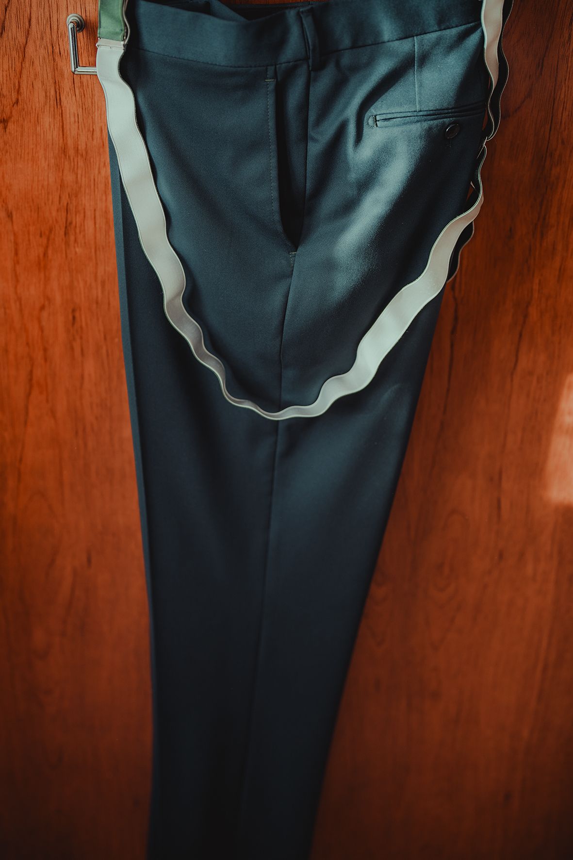 Close-up details of dark formal trousers hanging against wooden background.