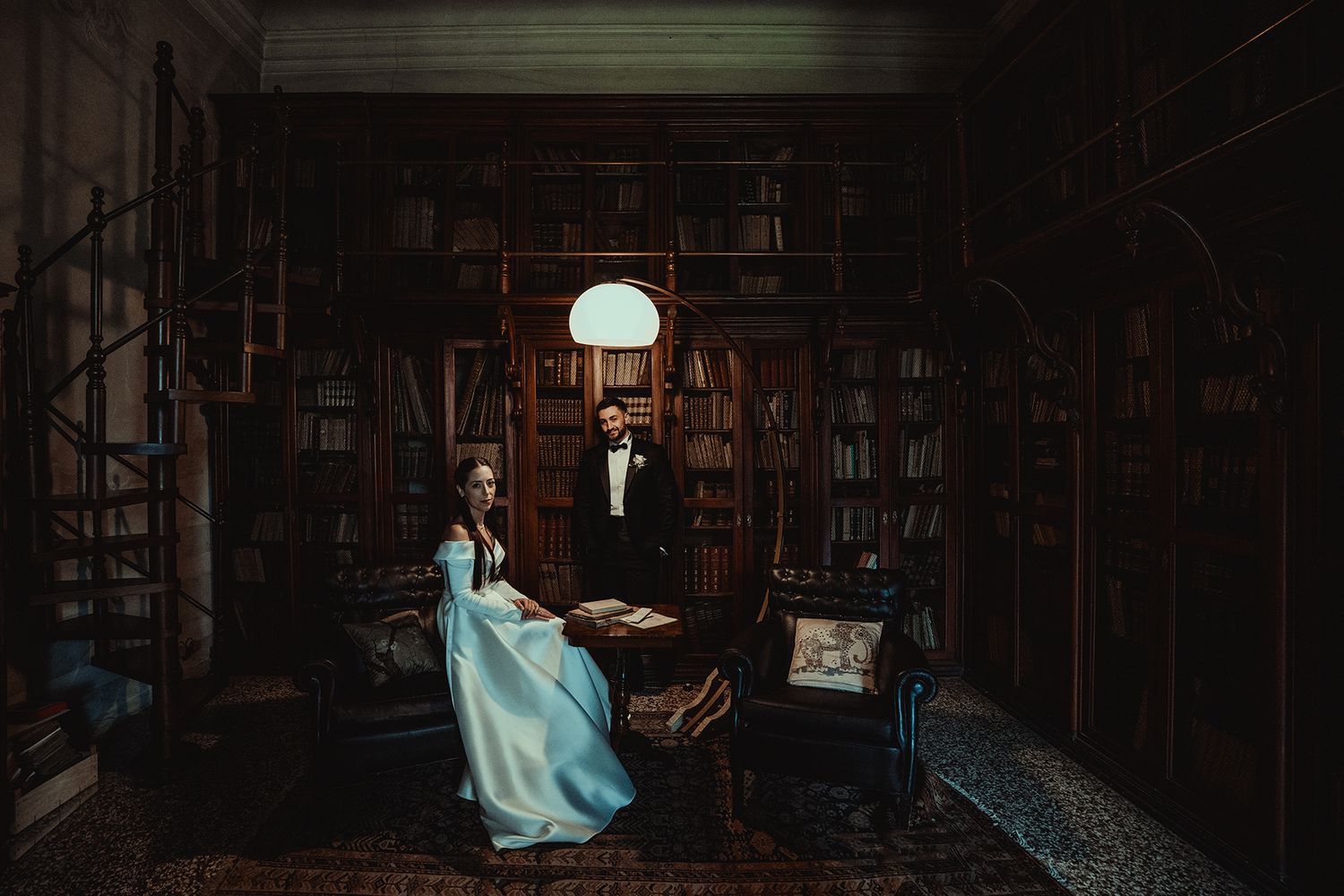 Dramatic lighting in a vintage library with rows of bookshelves and a white flowing dress.