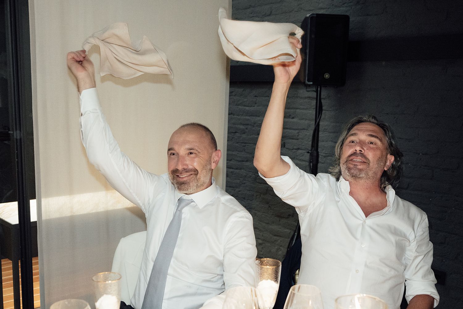 Wedding guests in white attire wave napkins enthusiastically during celebration.