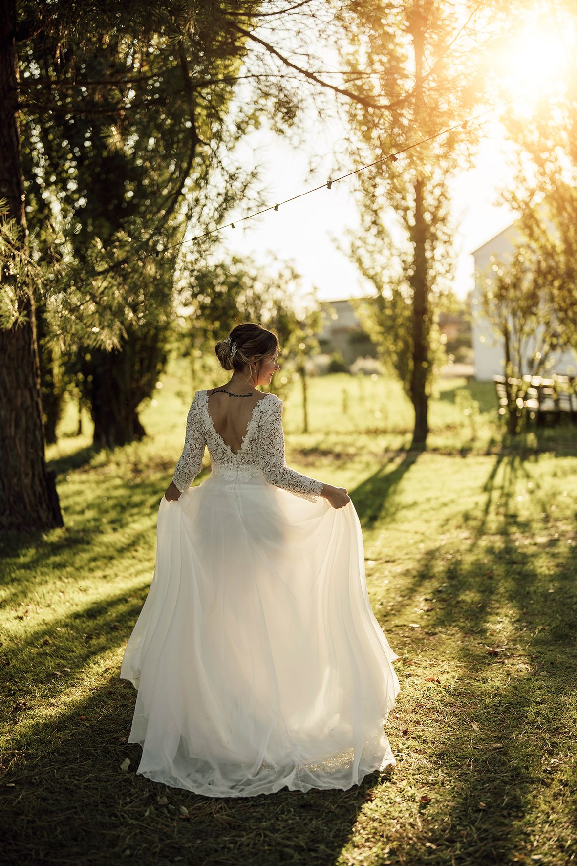 White wedding dress flowing in golden sunlight through trees at sunset.