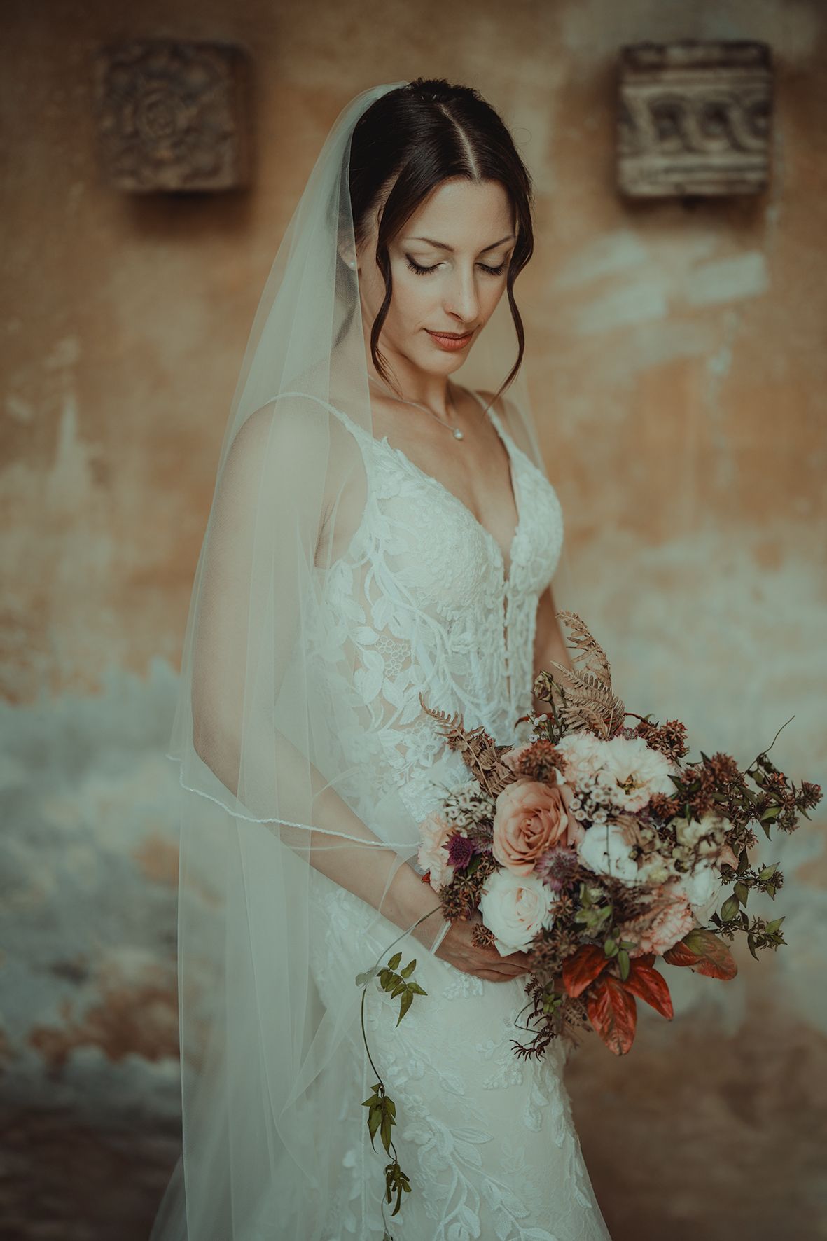 A bride in a lace wedding gown holds a romantic bouquet of roses and wildflowers.