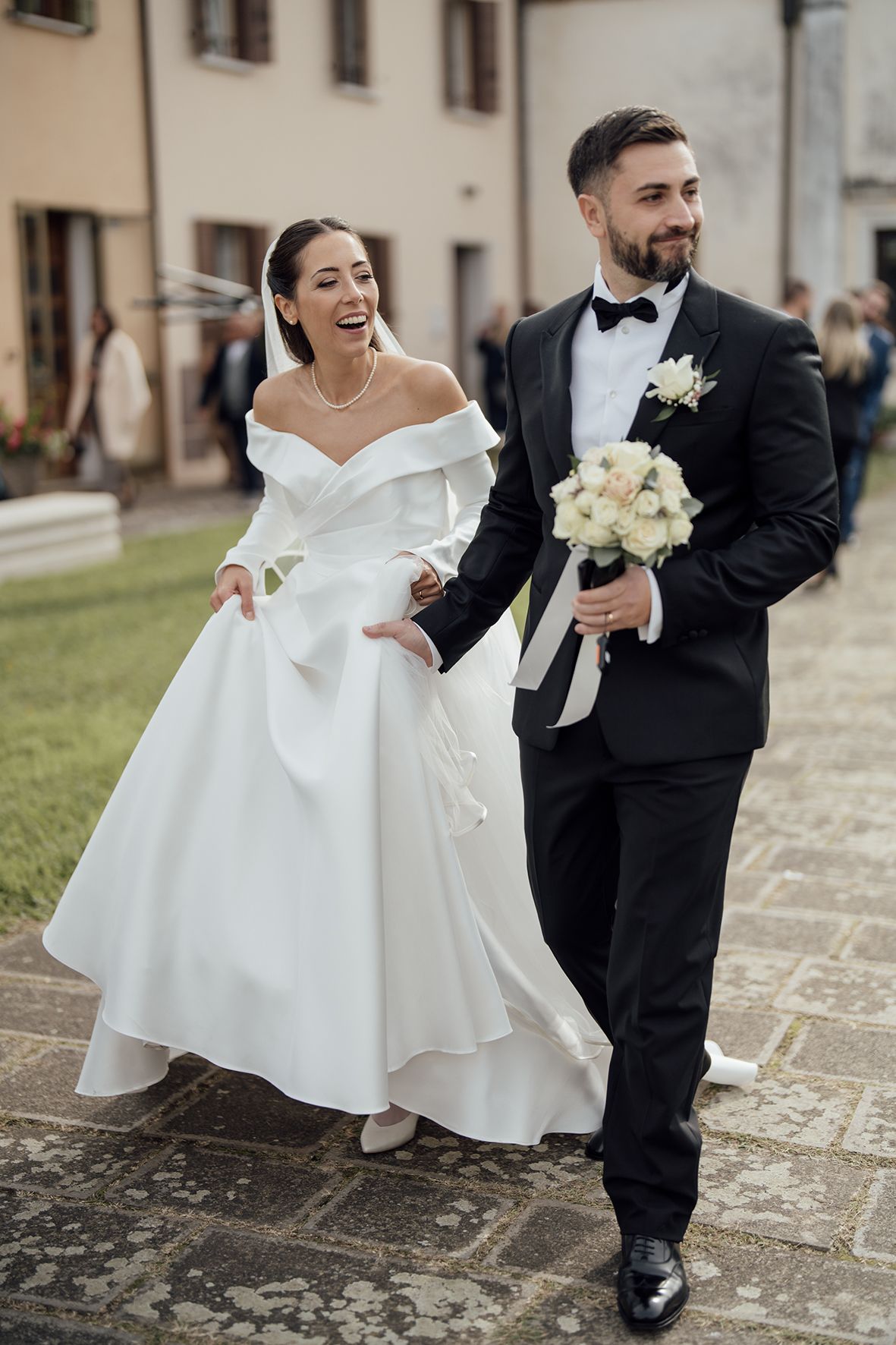 A joyful wedding couple walking together, with the bride in an elegant off-shoulder gown and groom in classic tuxedo.