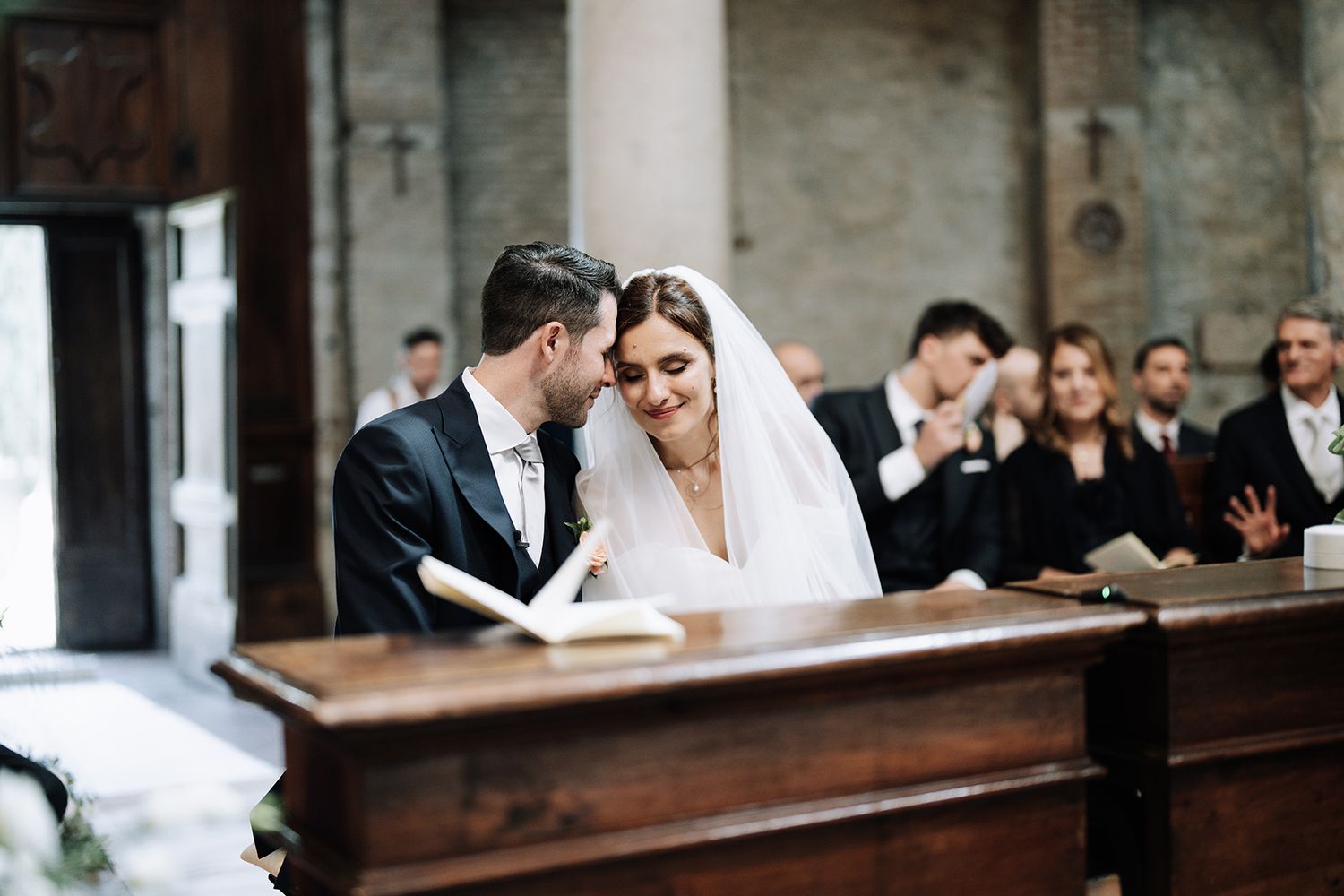 Intimate moment during church wedding ceremony with guests in background.