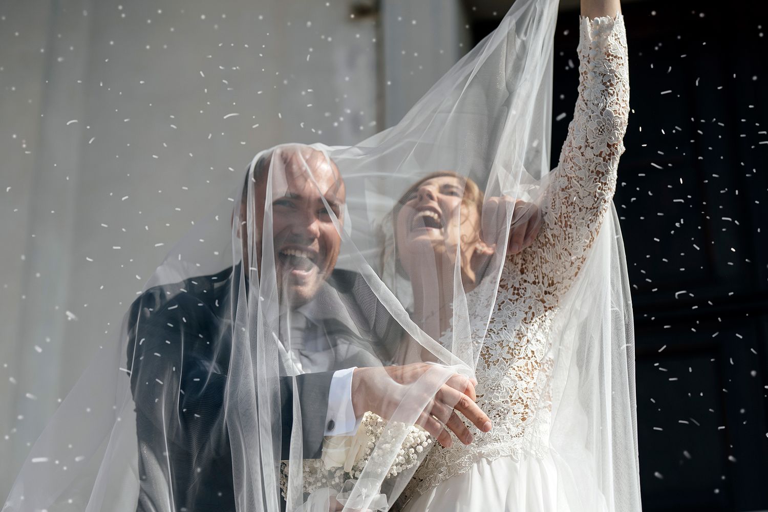 Bride with flowing veil shares intimate moment with groom under twinkling lights.