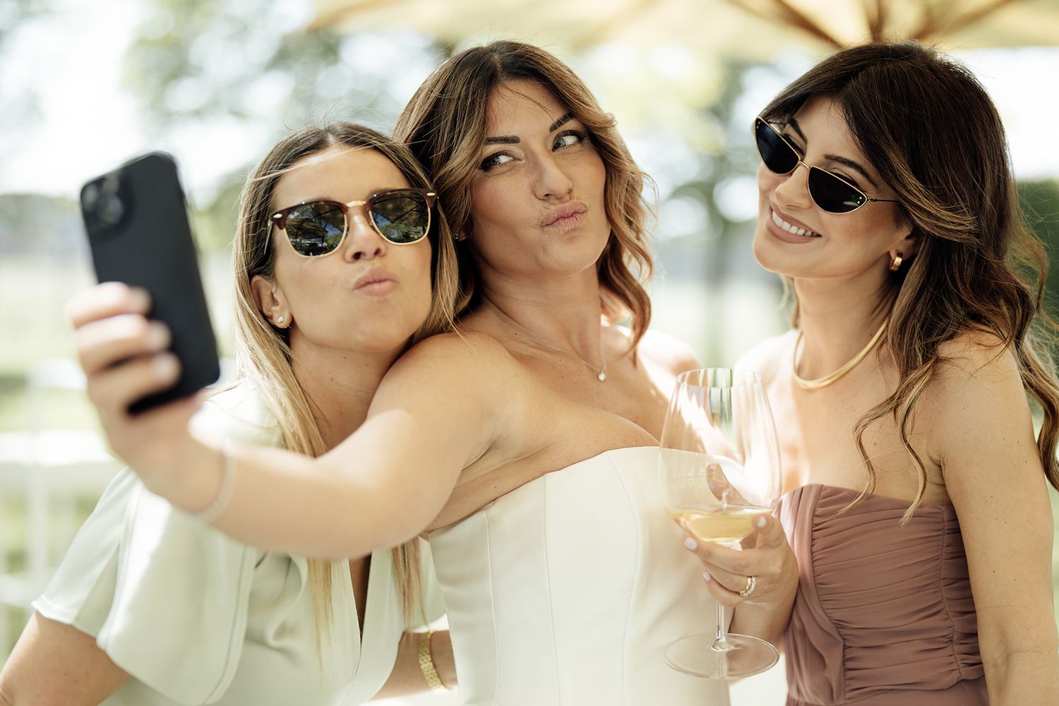 Wedding party members in sunglasses sharing laughs outdoors.