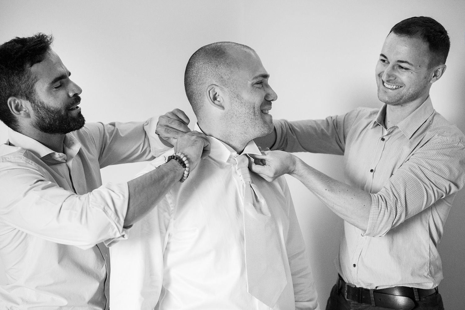 Groomsmen help adjust the groom's bowtie while sharing laughs together.