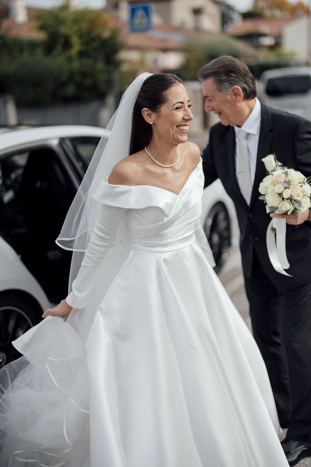 Elegant bride in a classic white wedding gown with dramatic collar detail and flowing veil holding a bouquet.