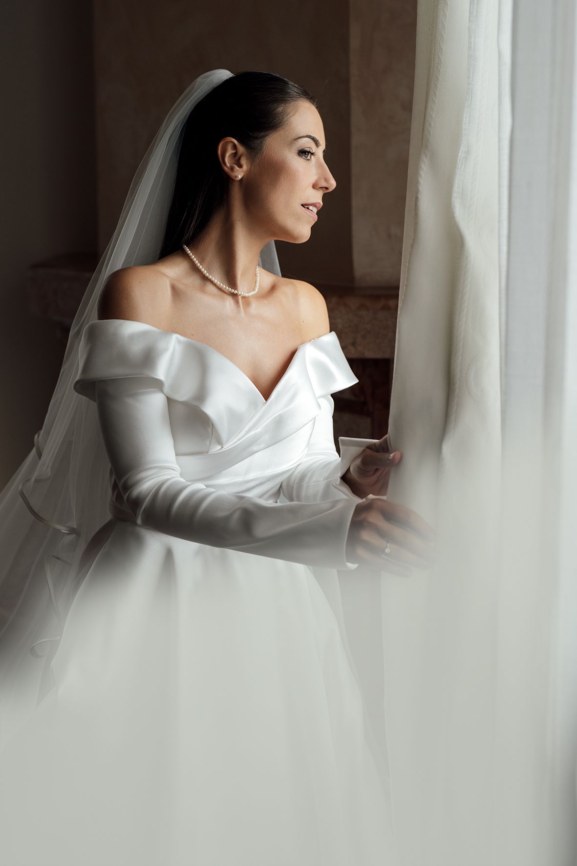 Elegant bridal portrait with soft window light and flowing white fabric.