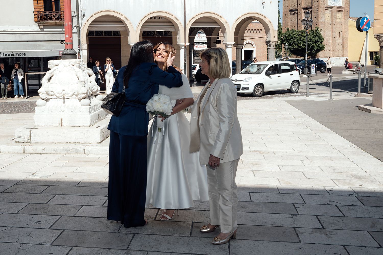 A wedding ceremony taking place outdoors in front of a historic stone building with white pillars and arches.