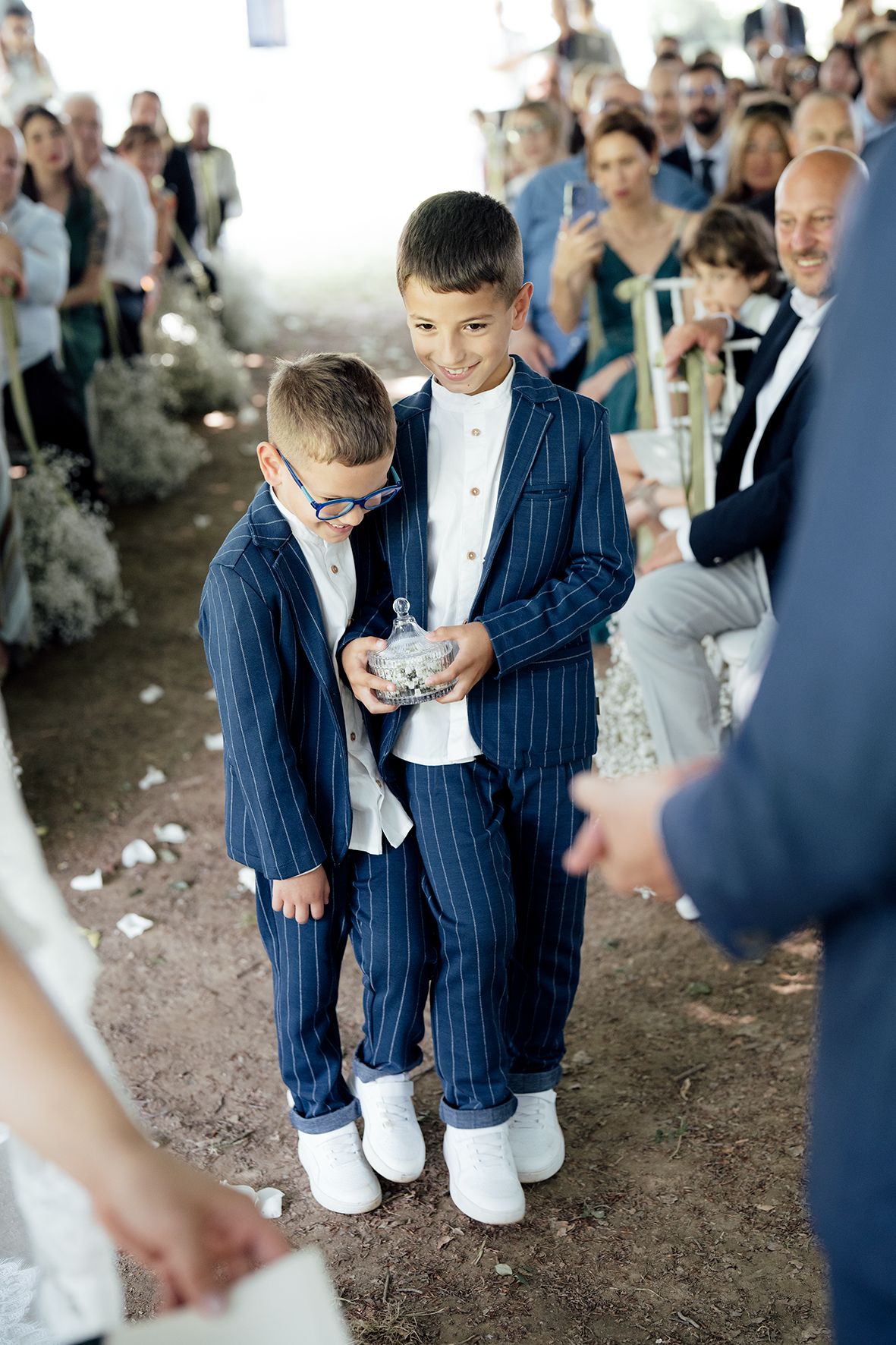 Children in matching navy suits and white sneakers at an outdoor wedding.