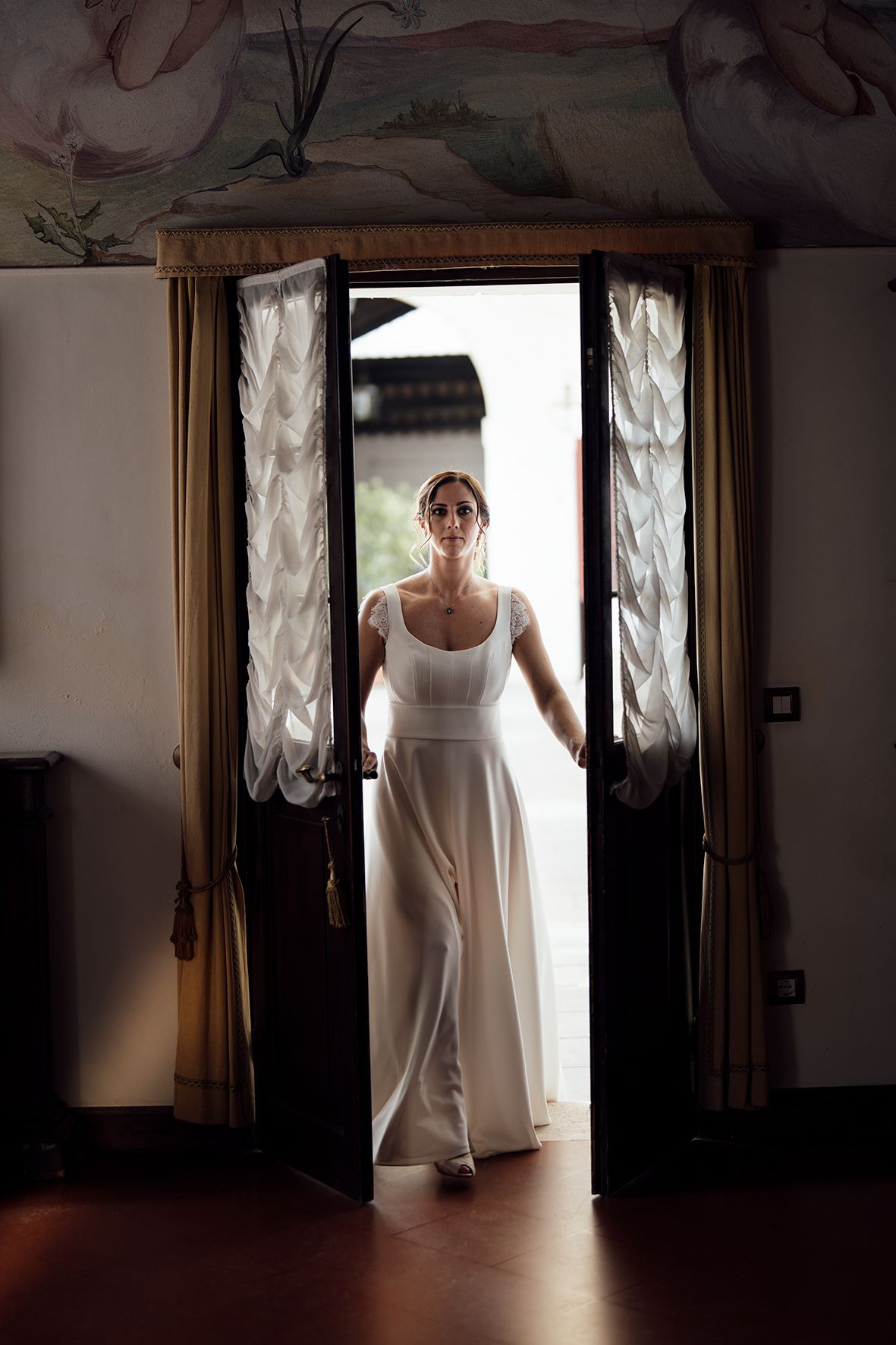 Dramatic silhouette sequence showing a figure emerging through a doorway in flowing white fabric.