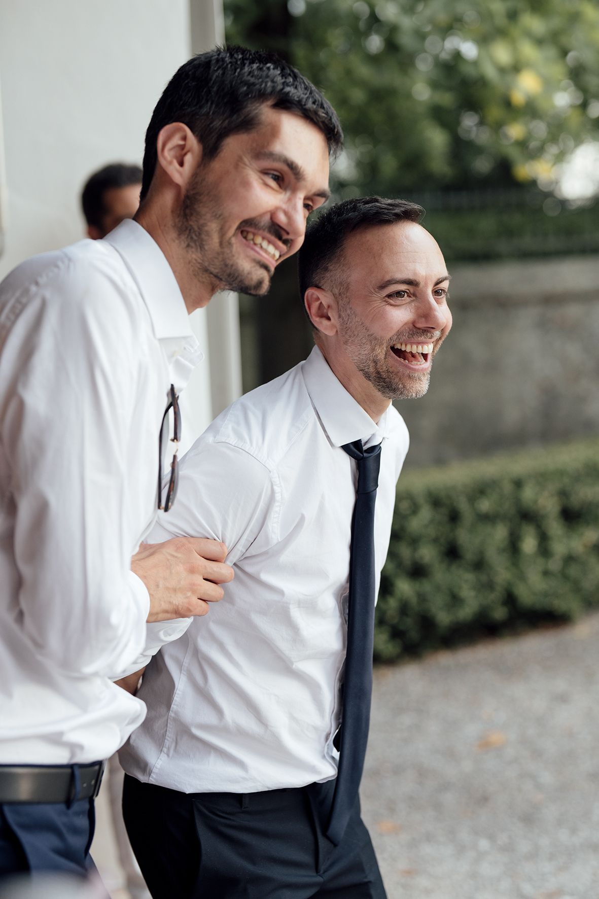 Groomsmen in white shirts and dark ties share laughs during wedding celebrations.