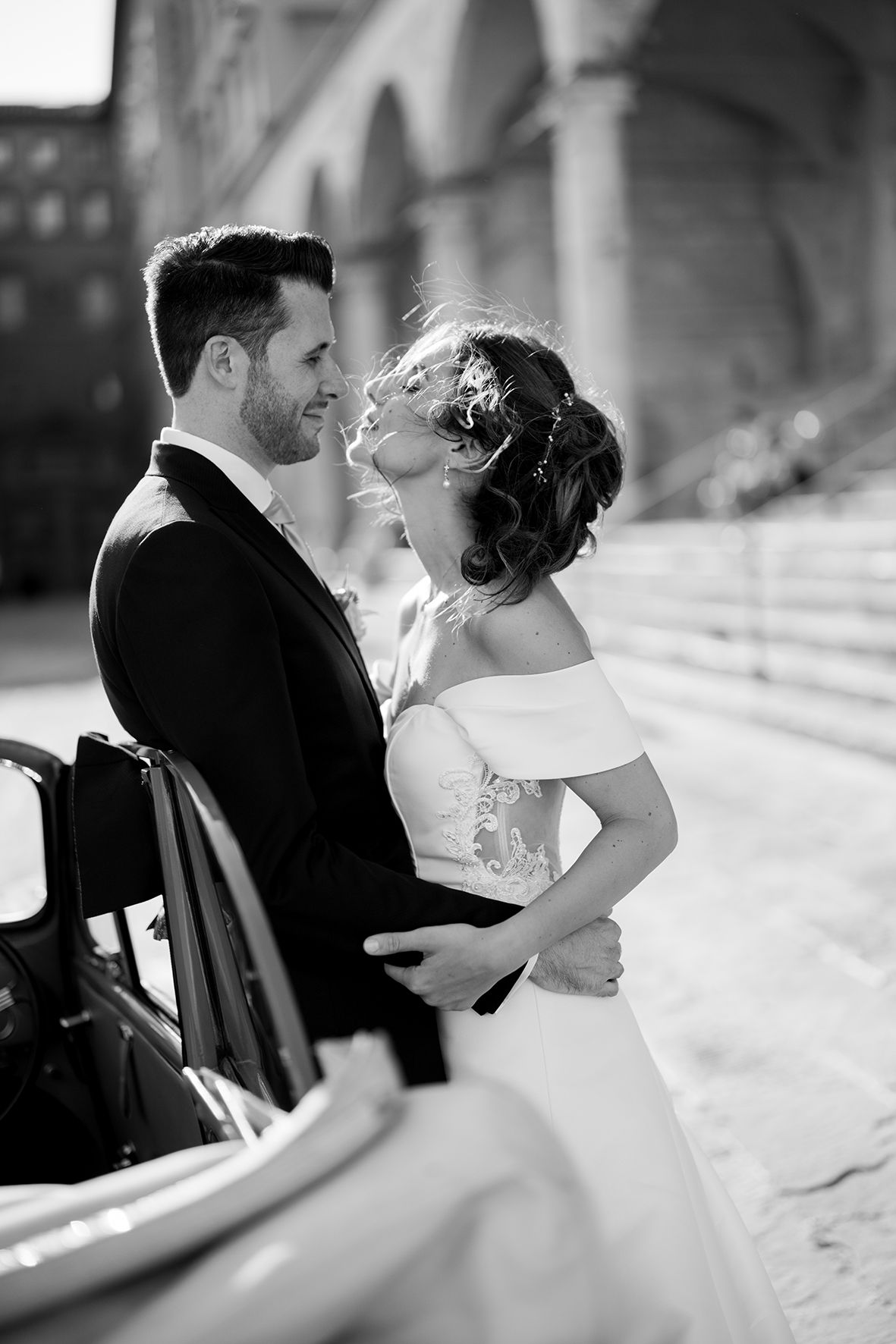 Black and white wedding photos capturing intimate moments between newlyweds by a classic car.