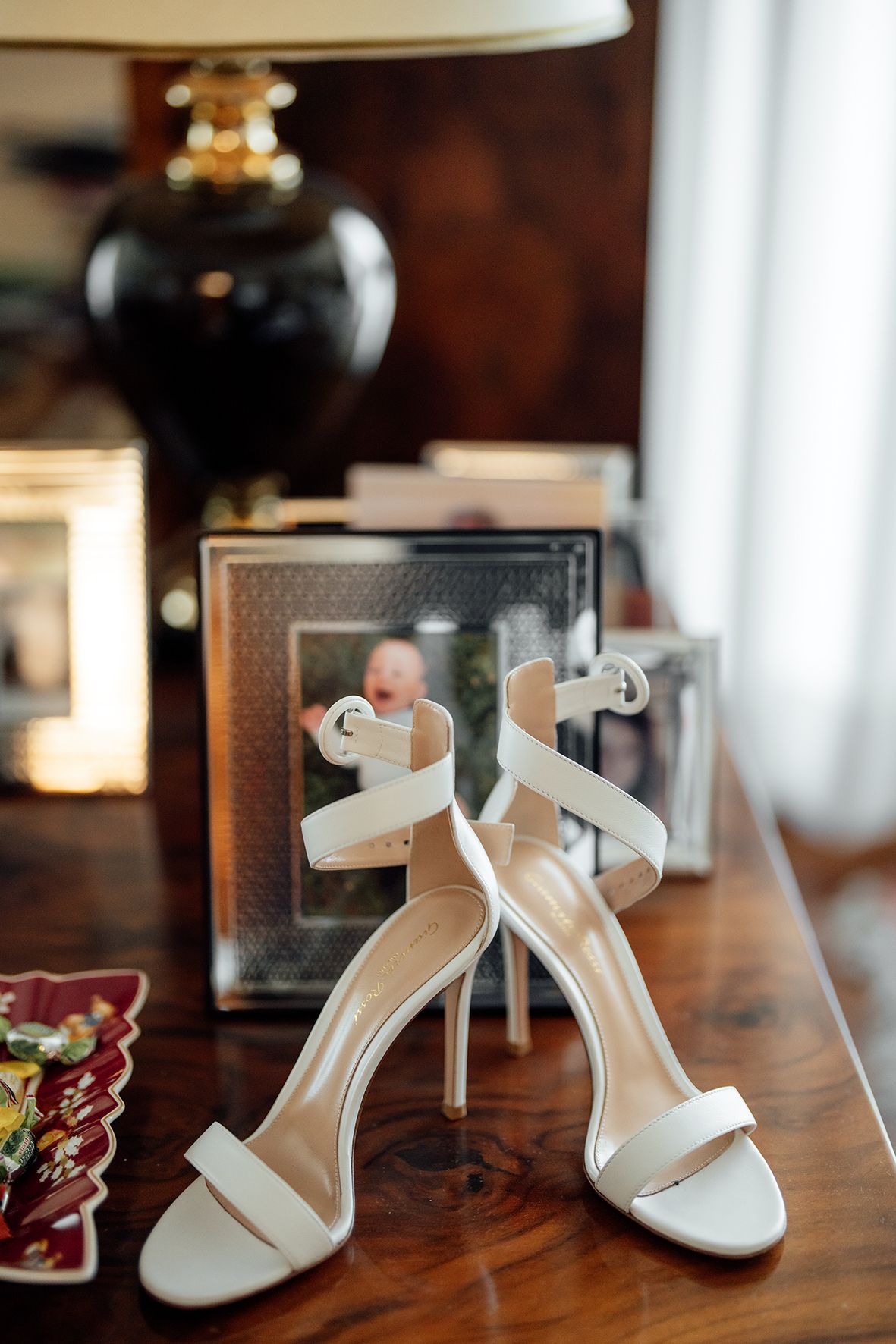 Elegant white bridal heels with ankle straps displayed on a wooden surface.