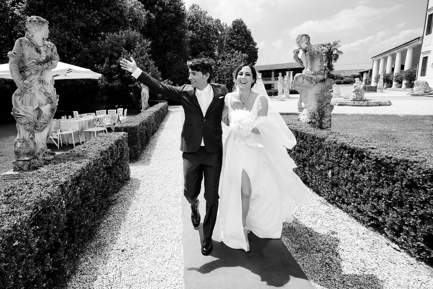 Wedding couple walking along a scenic path surrounded by manicured gardens and architecture.