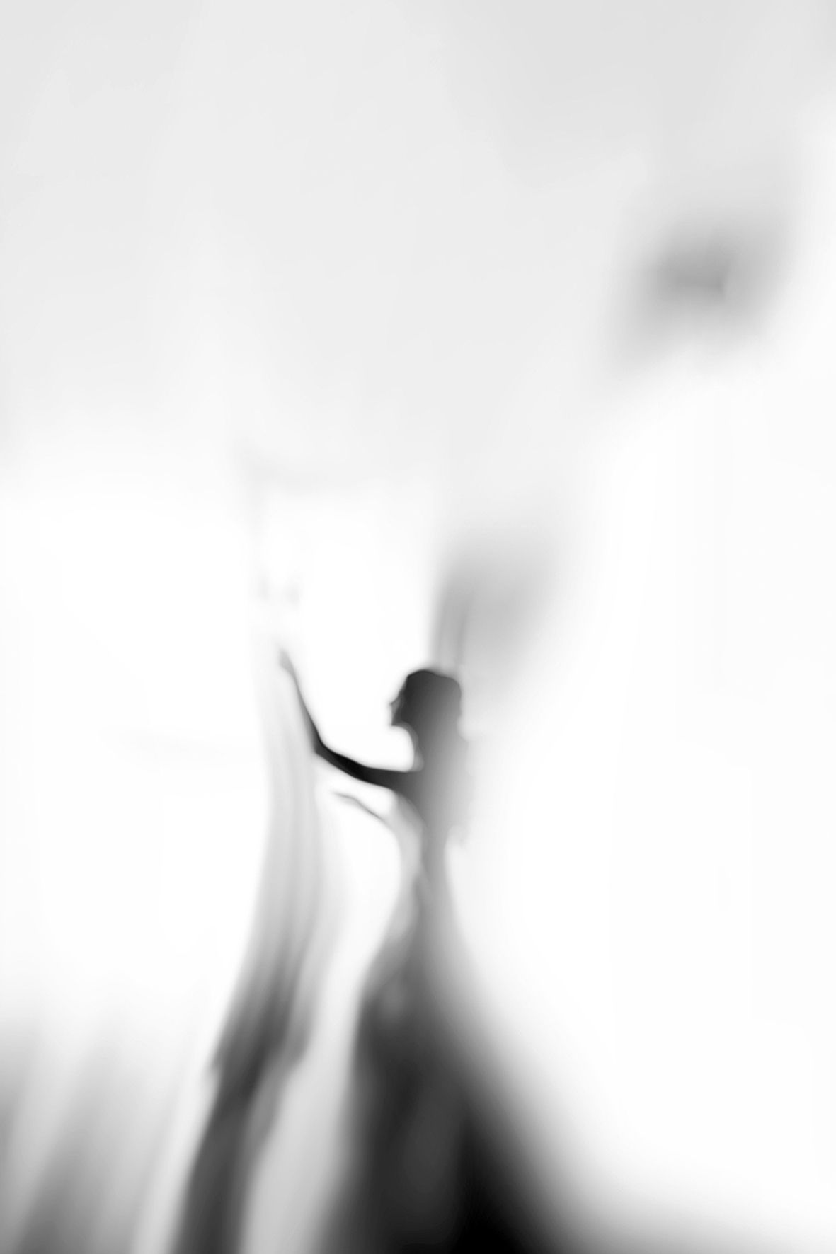A blurred black and white silhouette of a figure with raised arms creating an ethereal, dream-like artistic effect.