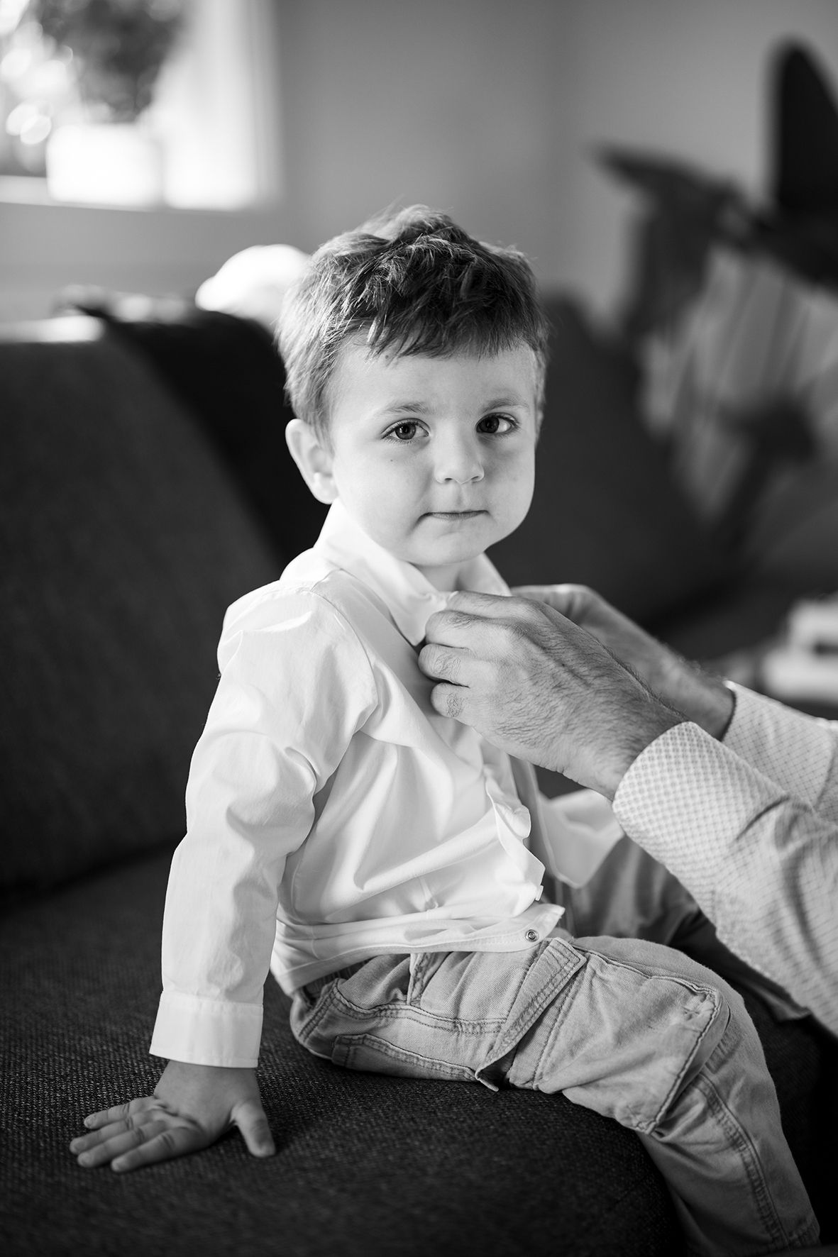 Black and white portrait of baby sitting on dark couch.