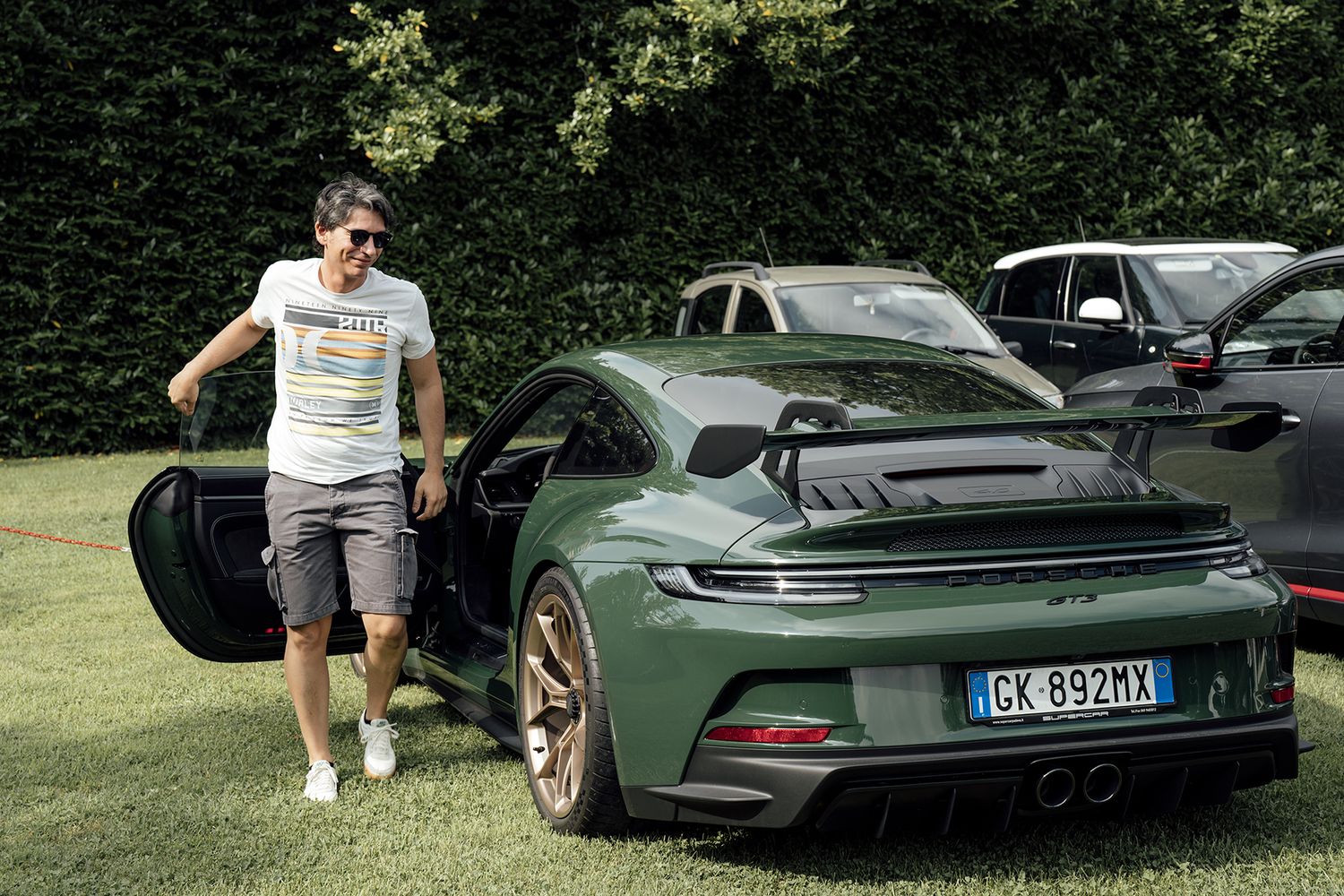 Person standing next to green Porsche sports car on grass.