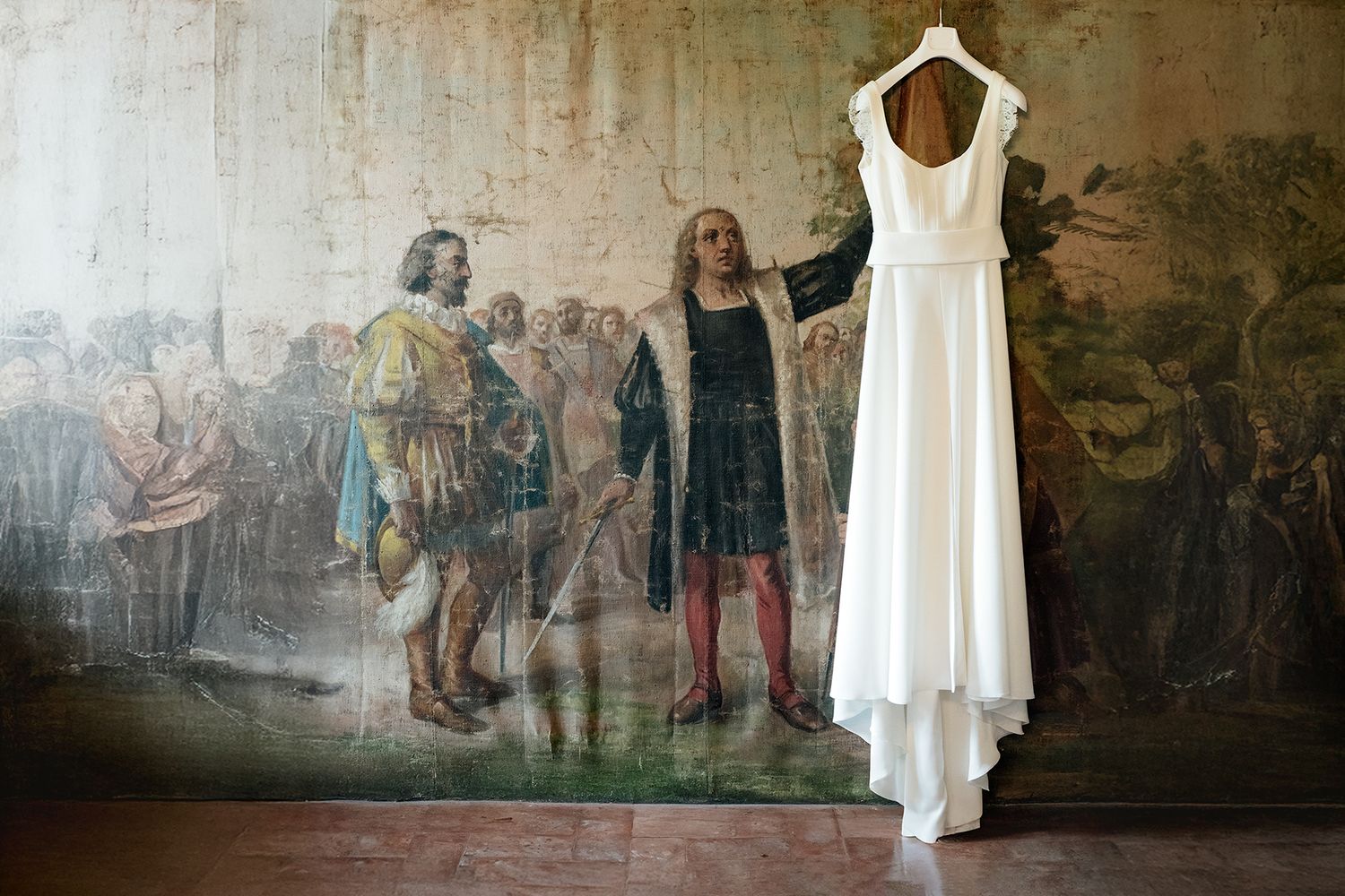White wedding dress hanging against wall with historical mural background.