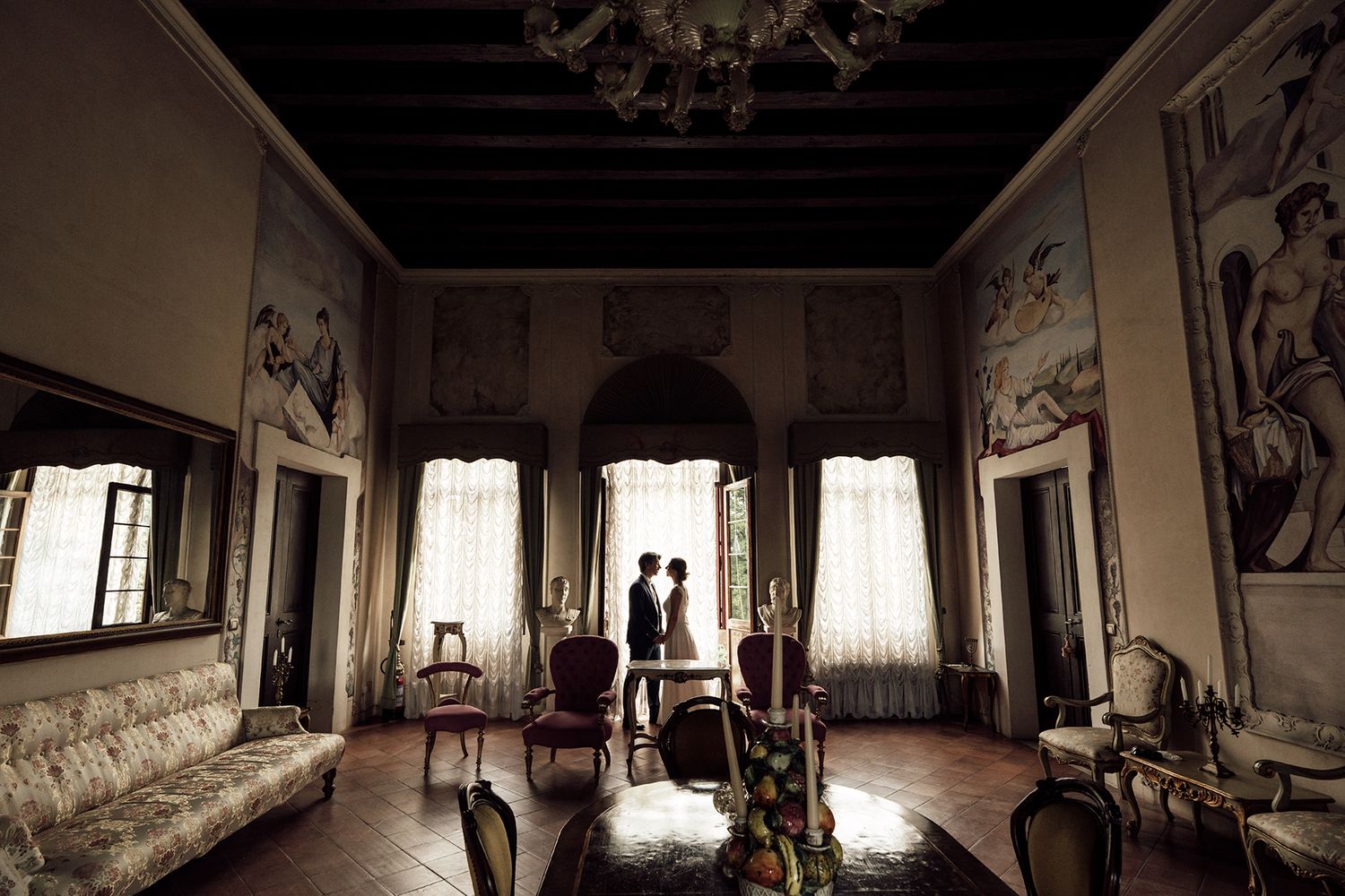 Panoramic view of an elegant room with large windows and classic furniture in warm lighting.