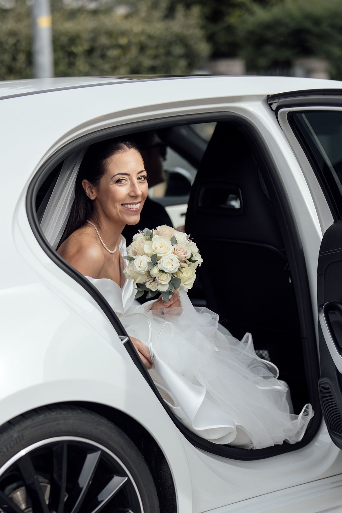 Radiant bride with white rose bouquet sitting in luxury car on wedding day.
