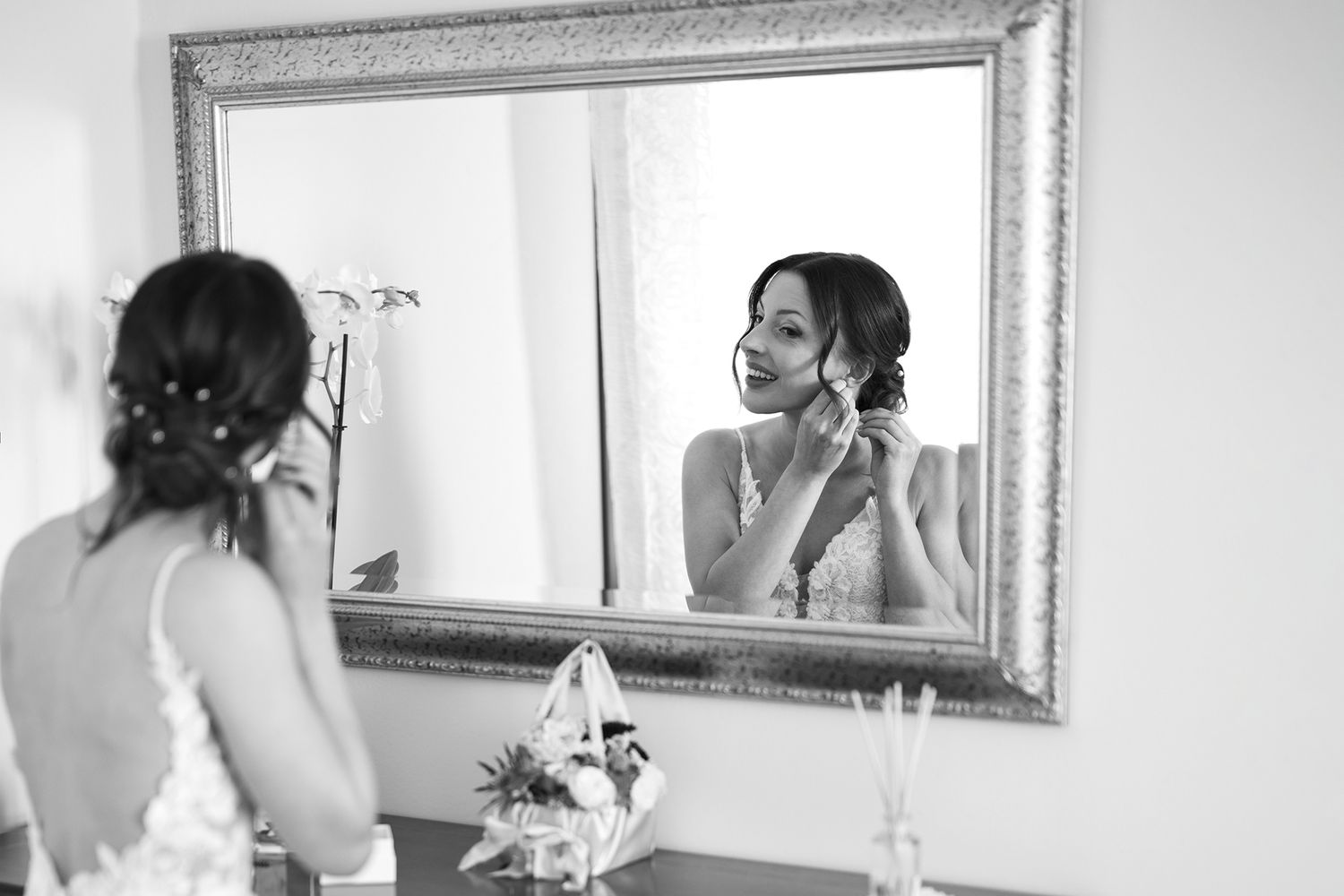 Black and white photo of bridal preparation moment at ornate mirror.