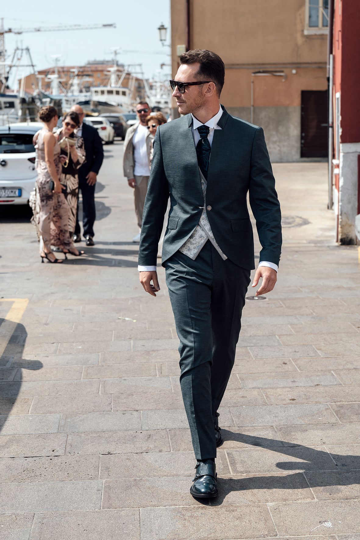 Men in formal suits walking on a stone paved outdoor plaza.