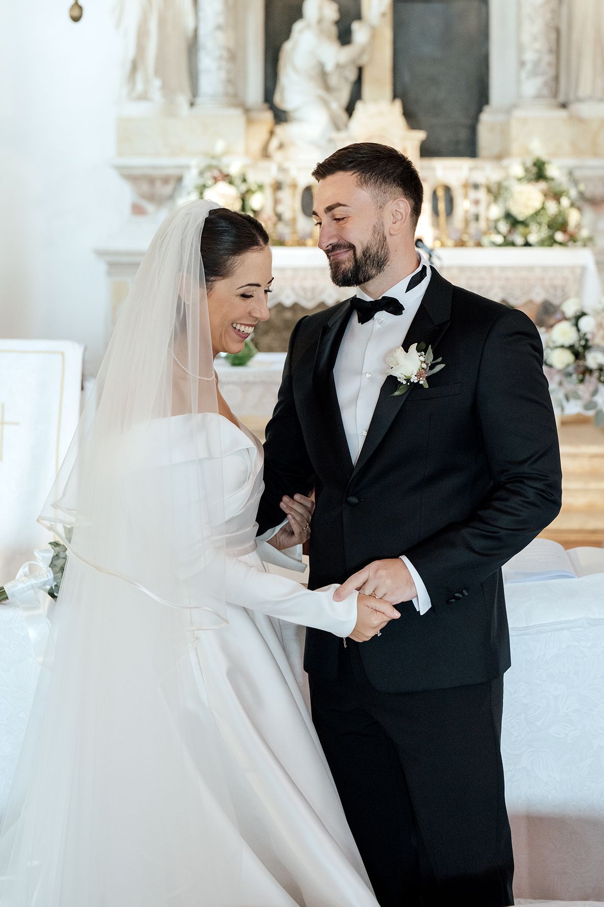 A candid moment of laughter between newlyweds in a beautifully decorated church with floral arrangements.