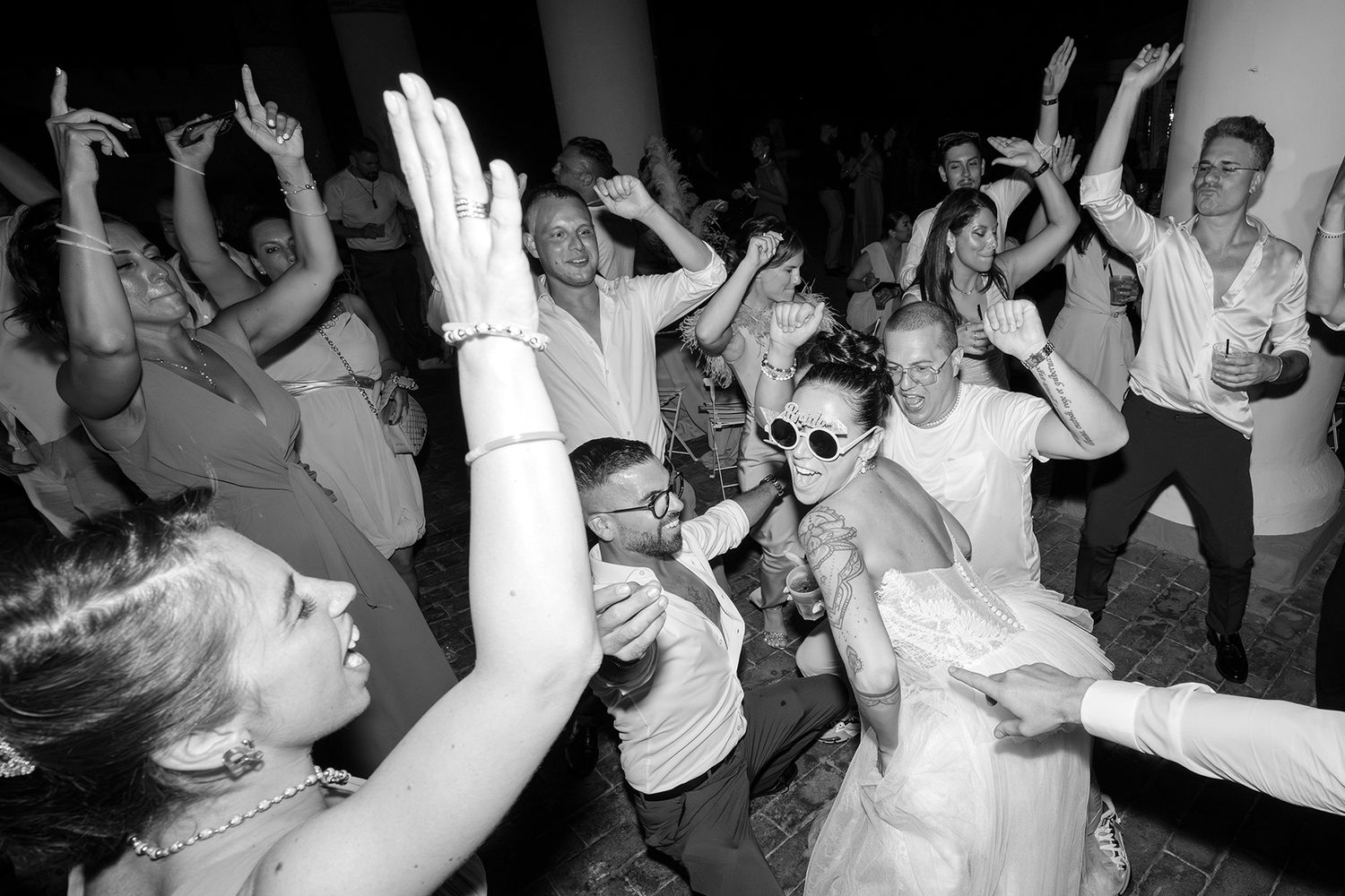 Black and white photos of wedding guests dancing and celebrating with raised arms.
