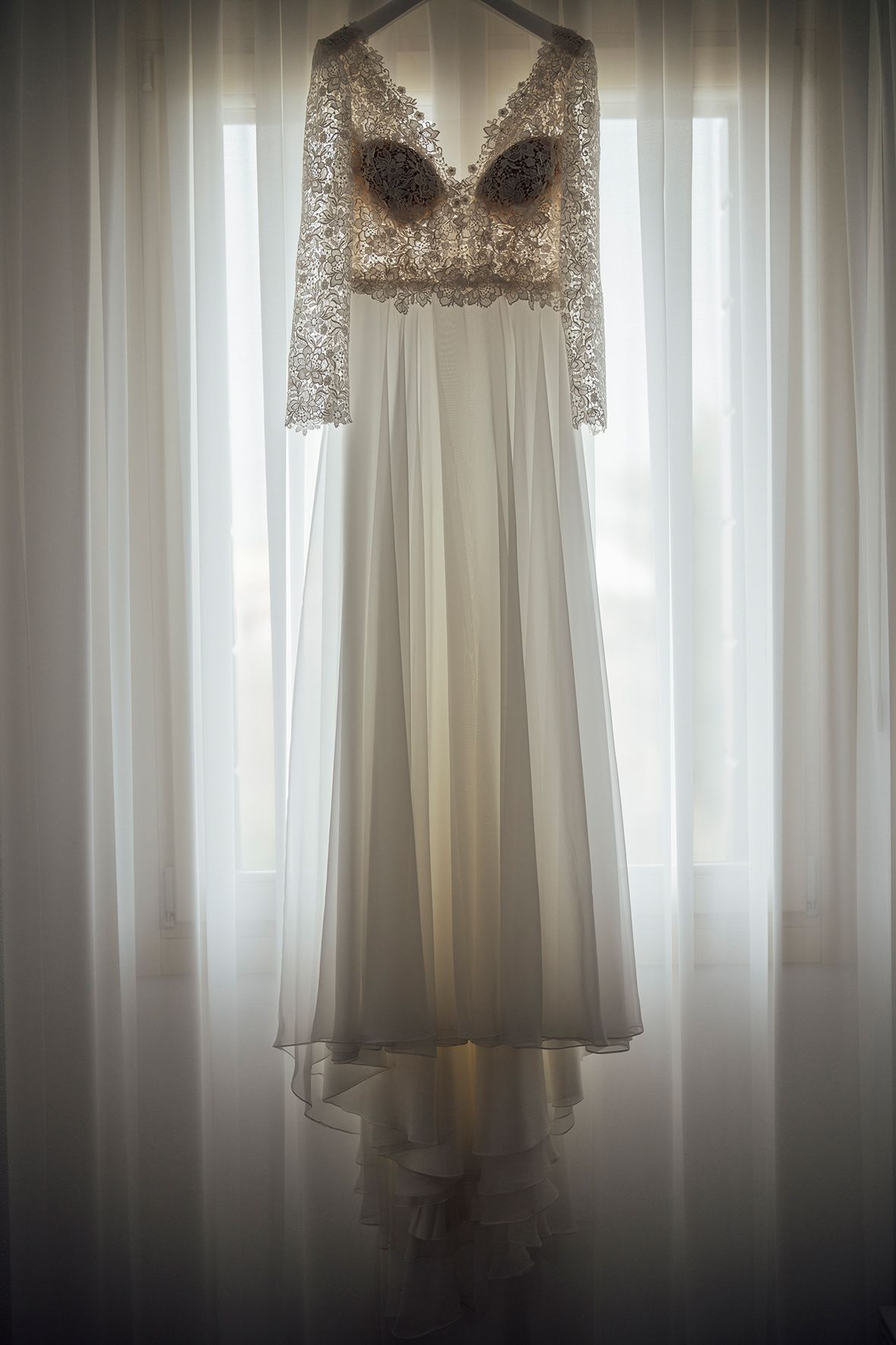White wedding dress hanging in front of a window with soft natural light creating an ethereal glow.
