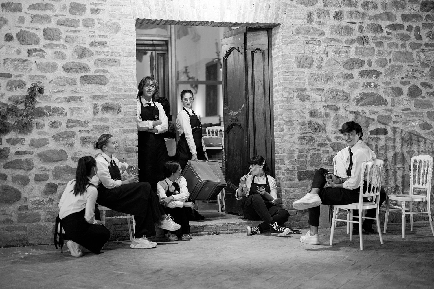 People sitting along a rustic stone wall during a wedding event.