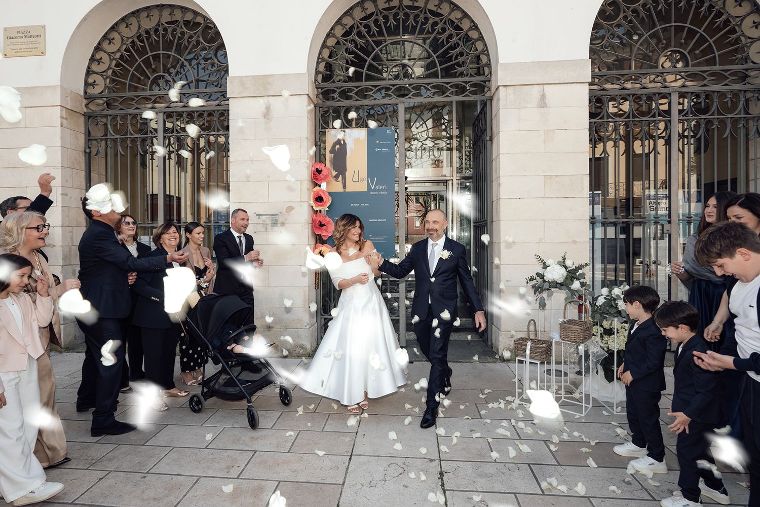 Newlyweds exit through ornate arched doorways as guests throw confetti in celebration.