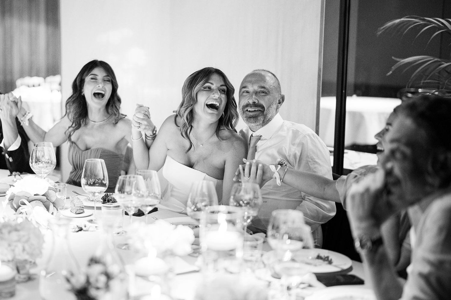 Wedding reception guests laugh and celebrate at dining tables.