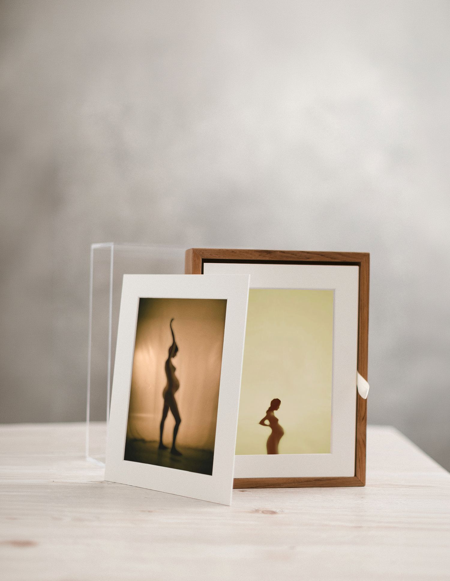 Two framed artistic silhouette photos displayed on a wooden surface, one in a walnut frame and one in a clear acrylic frame.